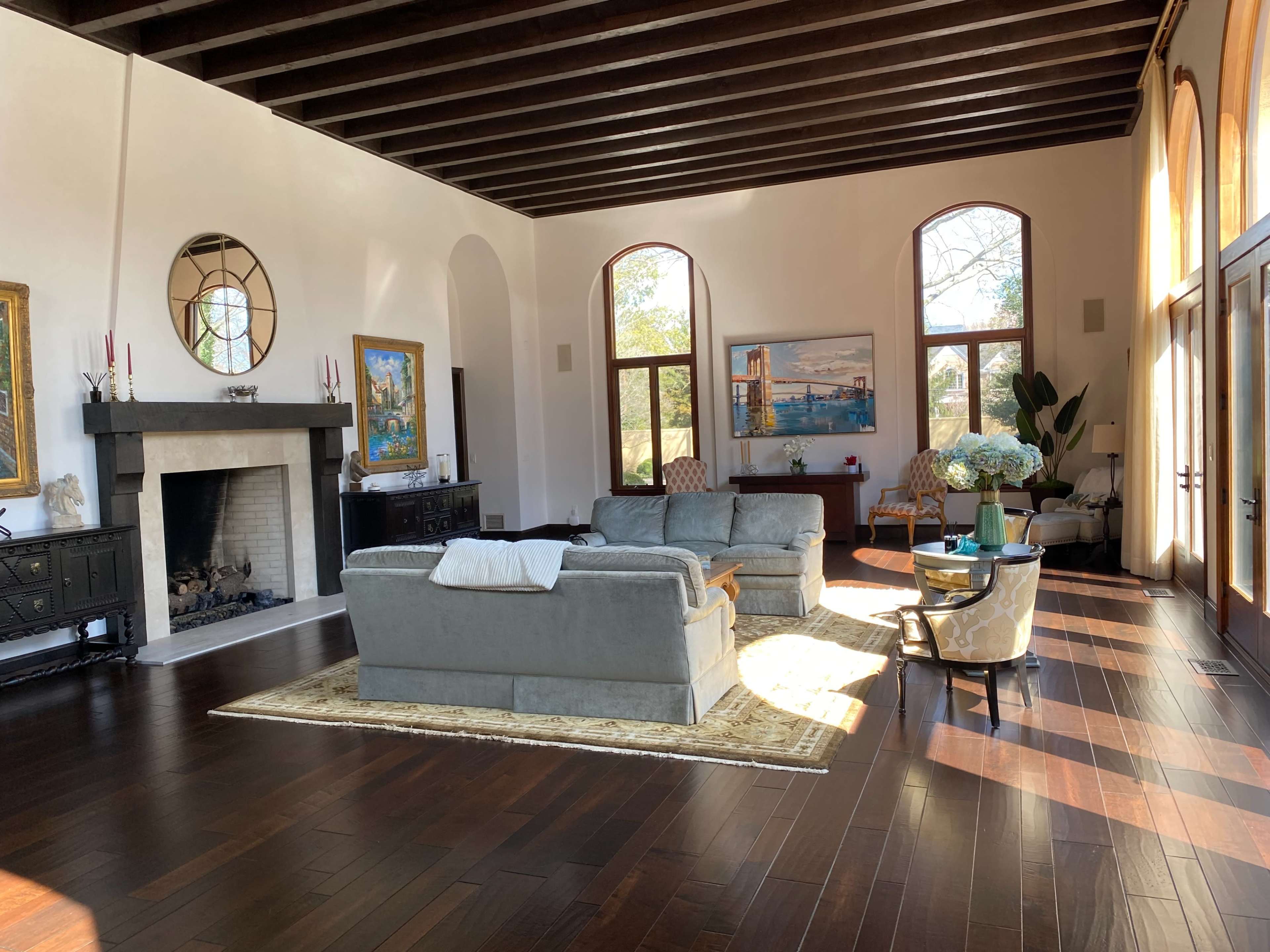 A spacious living room features a fireplace, large windows, and stylish furniture arranged around a coffee table.