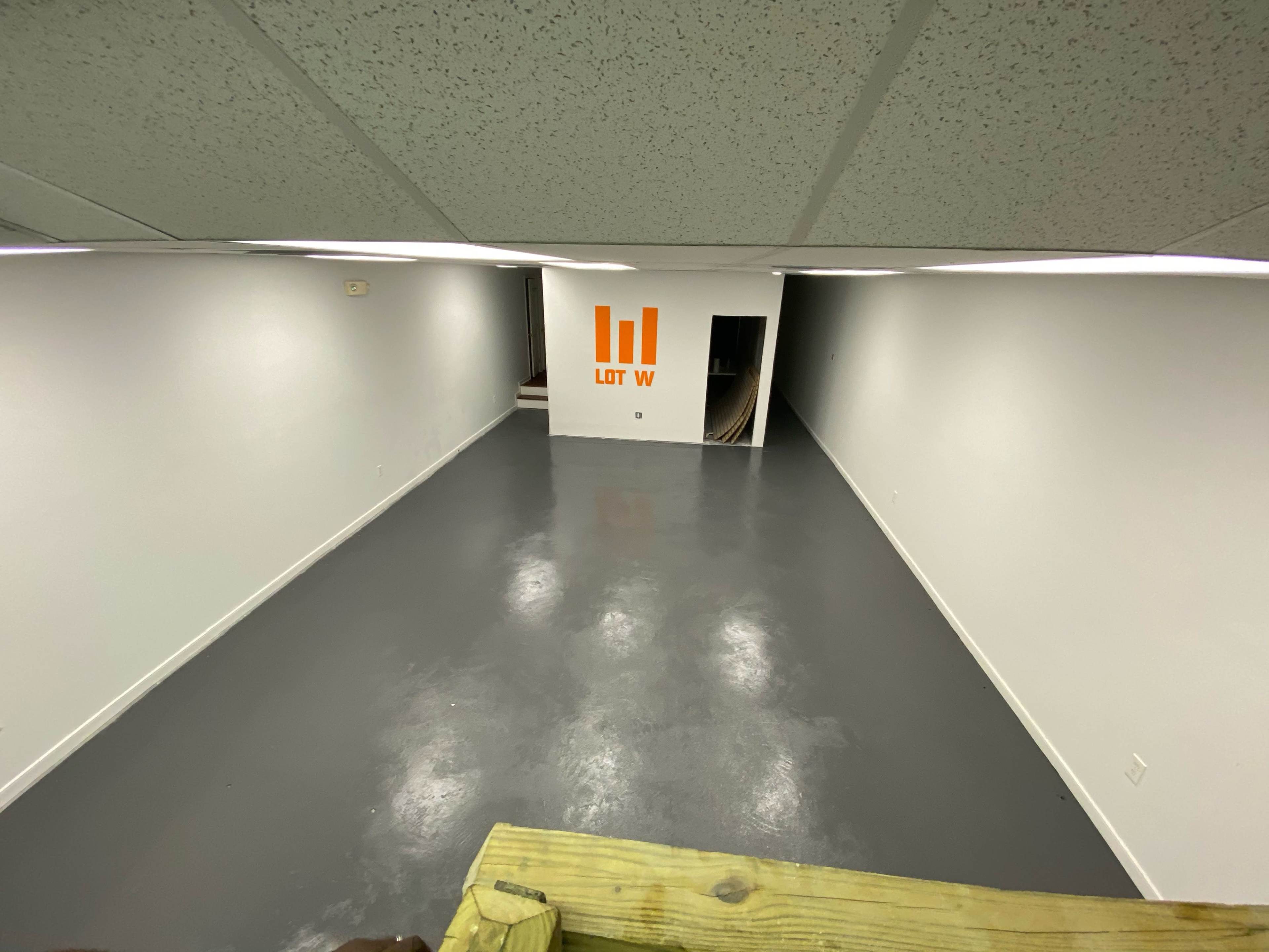 An empty, well-lit room with a gray floor and a wall featuring an orange logo that reads "LIT W."