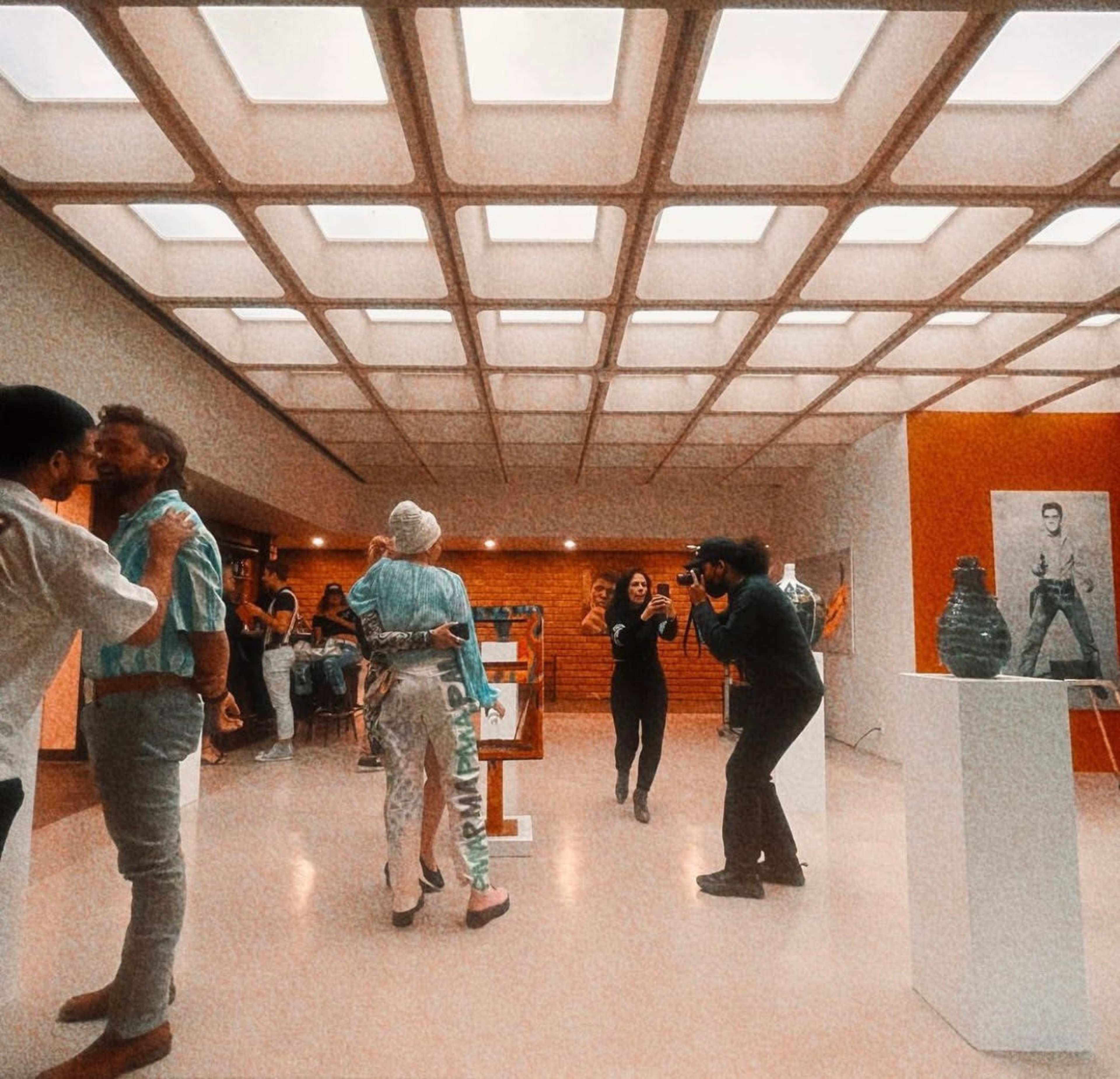 A group of people is interacting and taking photographs in an art gallery featuring various artworks, including paintings and sculptures.