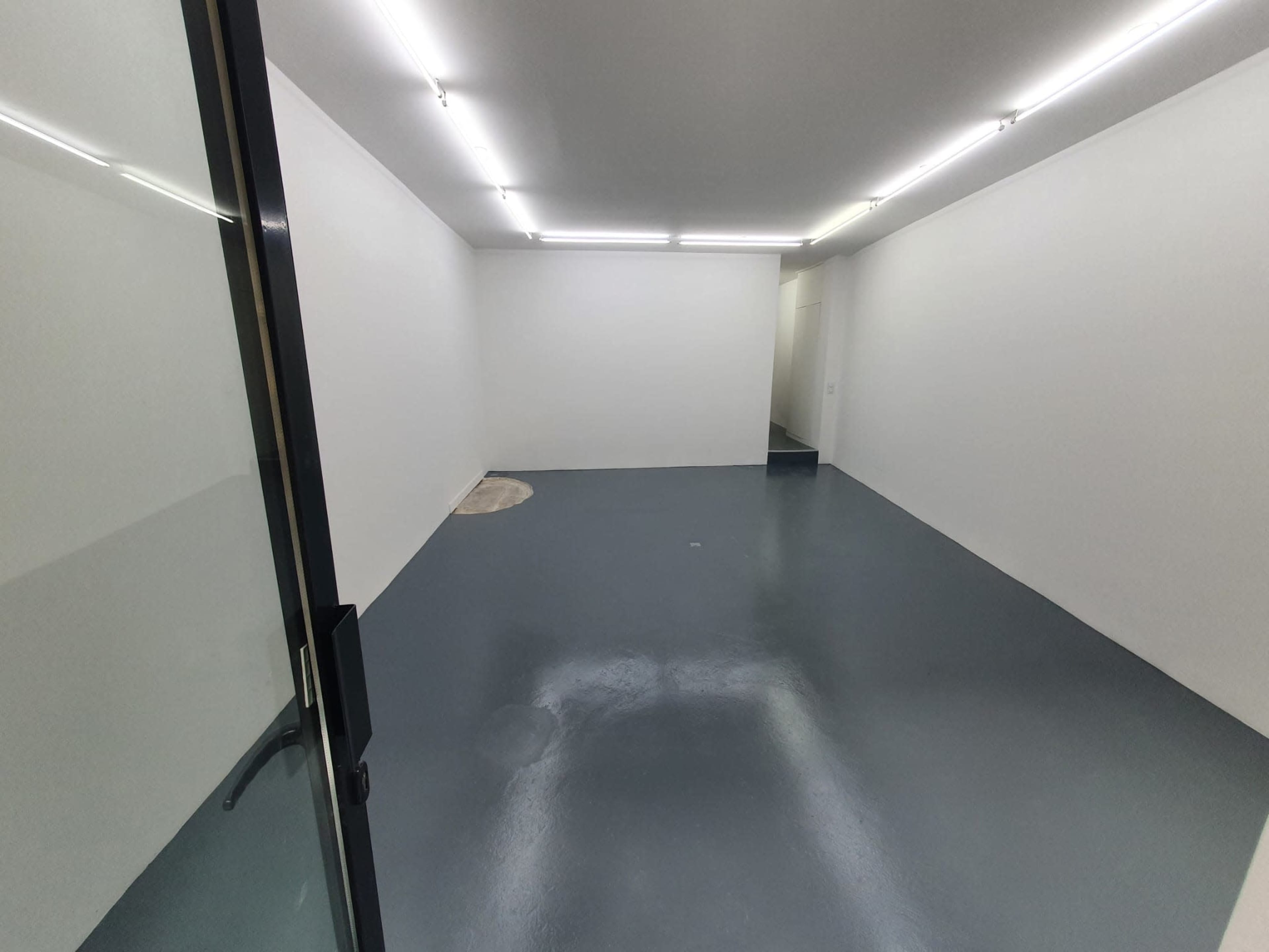 An empty room with a smooth gray floor and white walls, illuminated by overhead lighting.