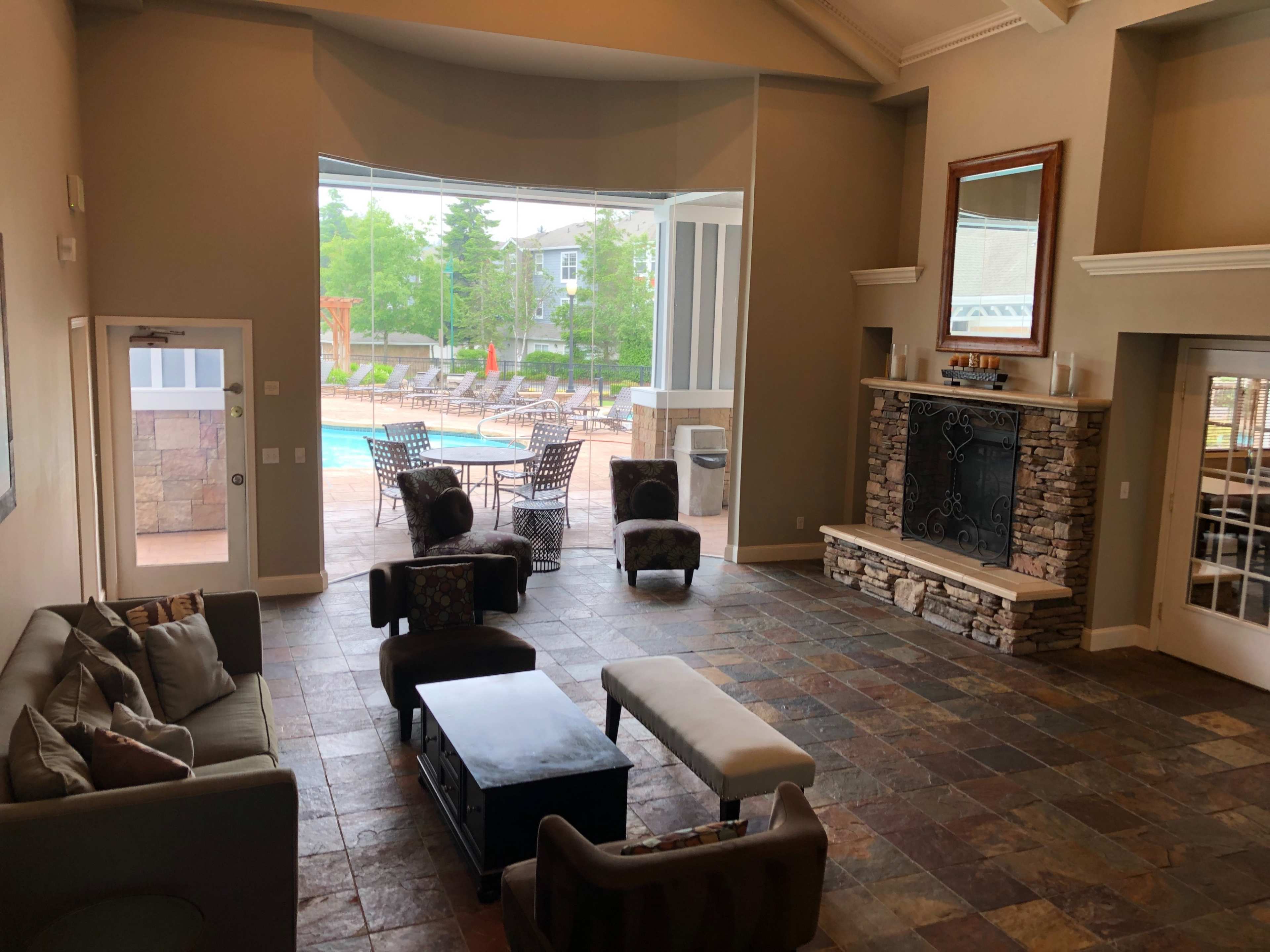 A spacious lounge area with a stone fireplace, modern furniture, and large windows overlooking an outdoor pool area.