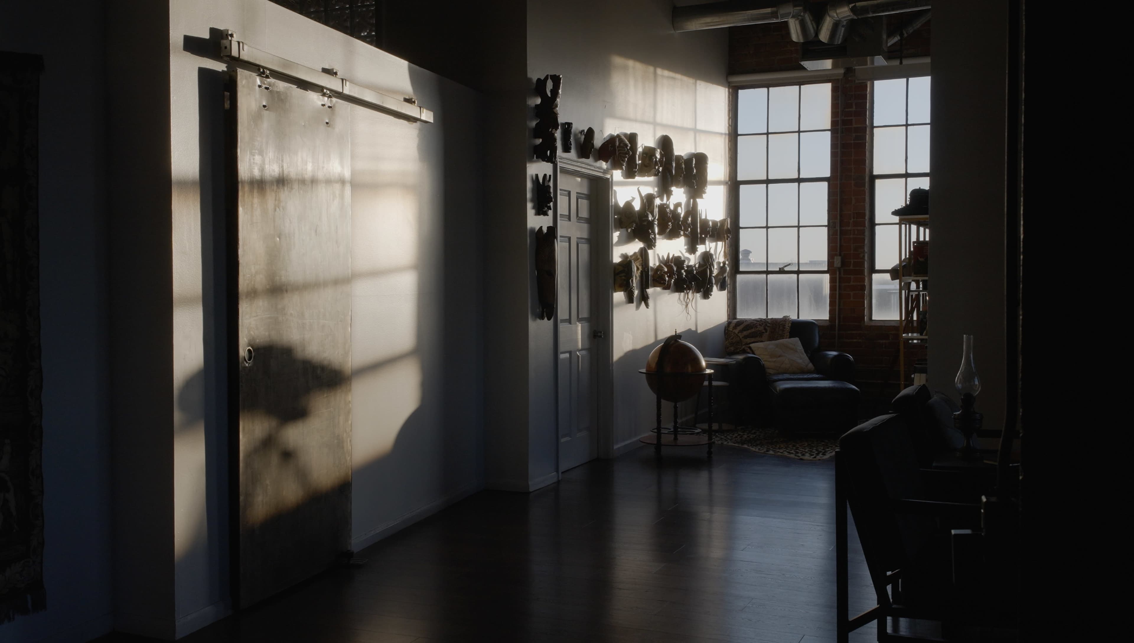 The image shows a well-lit interior space with a large window, a sliding barn door, and artwork displayed on the walls.