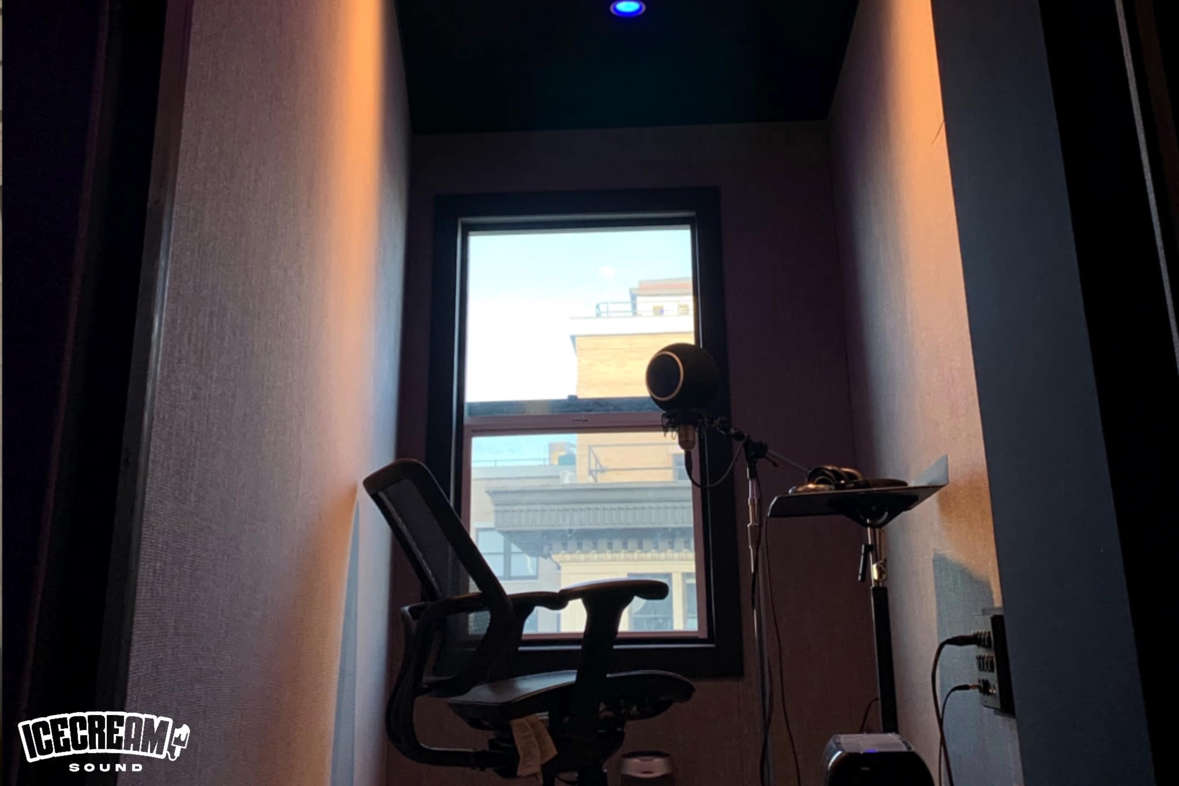 A small room features a chair facing a window with a microphone and stand nearby.
