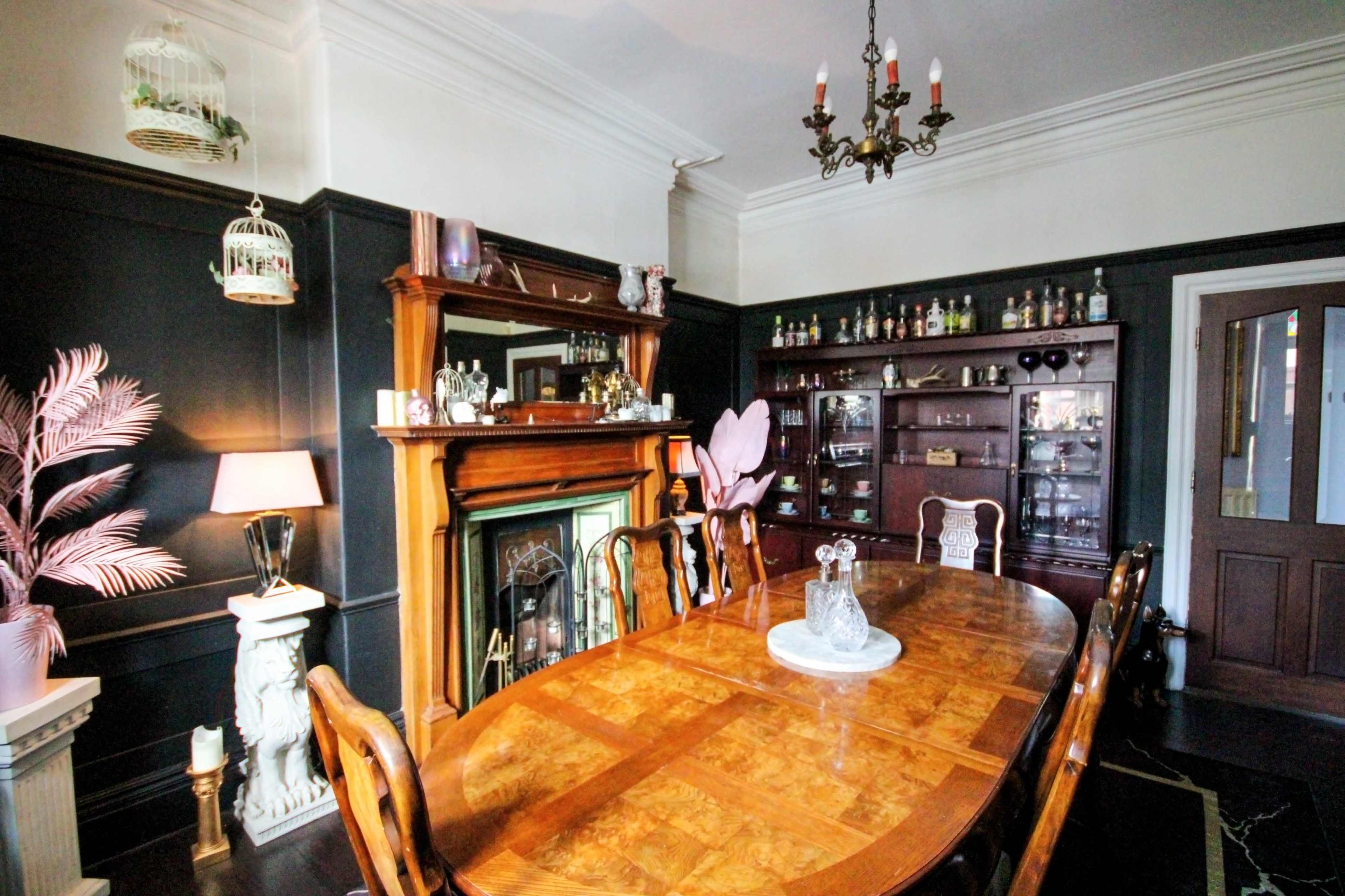 A dining room with a large wooden table set for meals, surrounded by chairs, and features a fireplace, display cabinets, and decorative elements.
