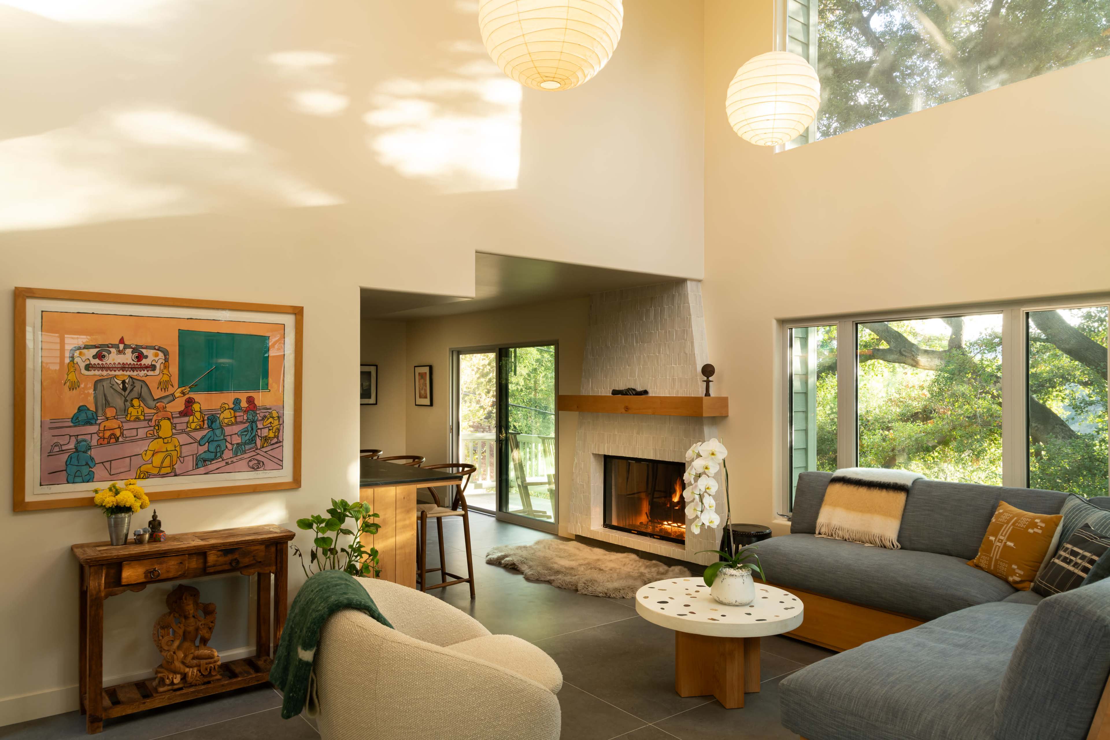 A bright living room features large windows, a fireplace, and a mix of modern and artistic furniture.