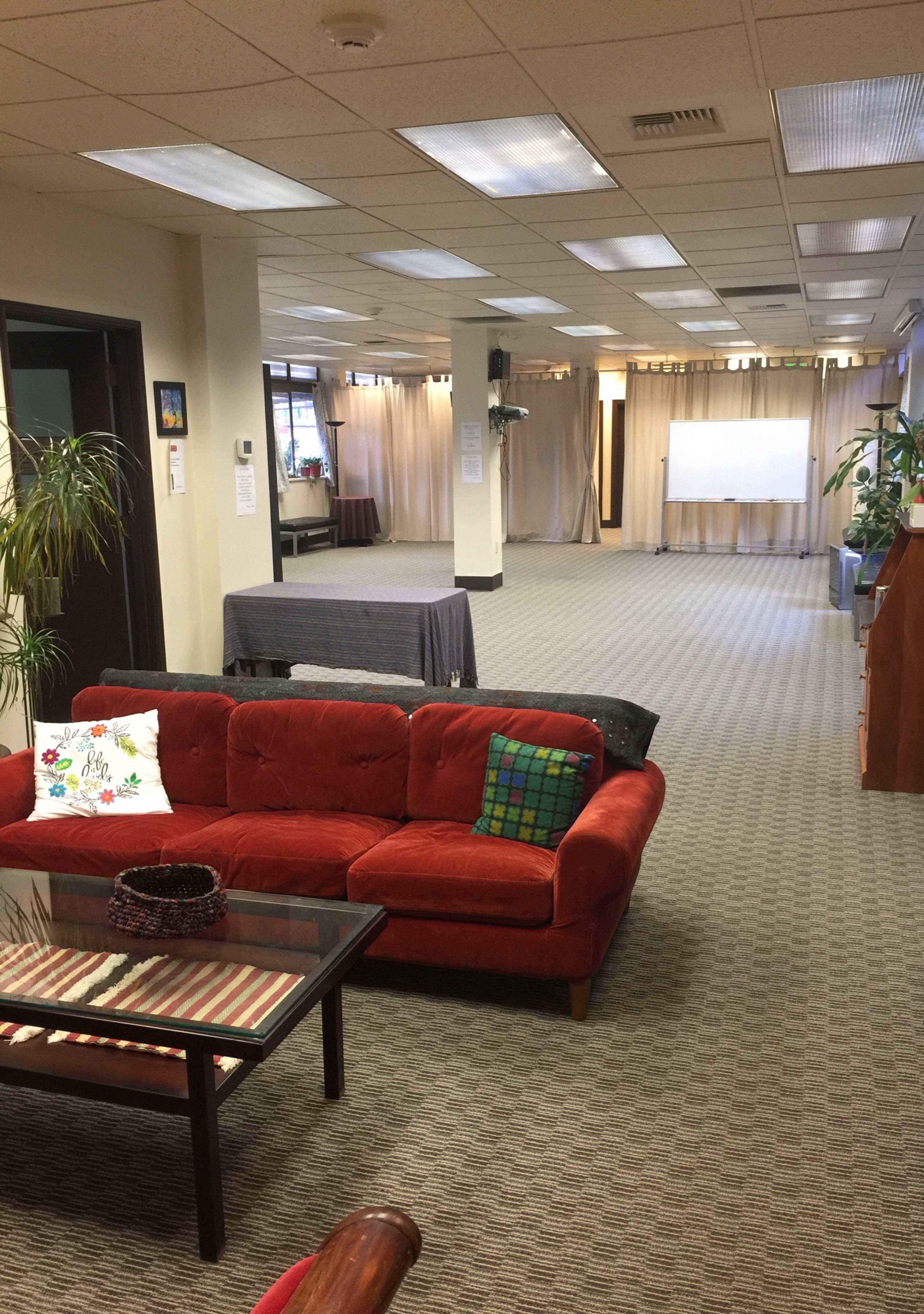 A spacious, well-lit room with a red sofa, various plants, and gray tables arranged for an event.