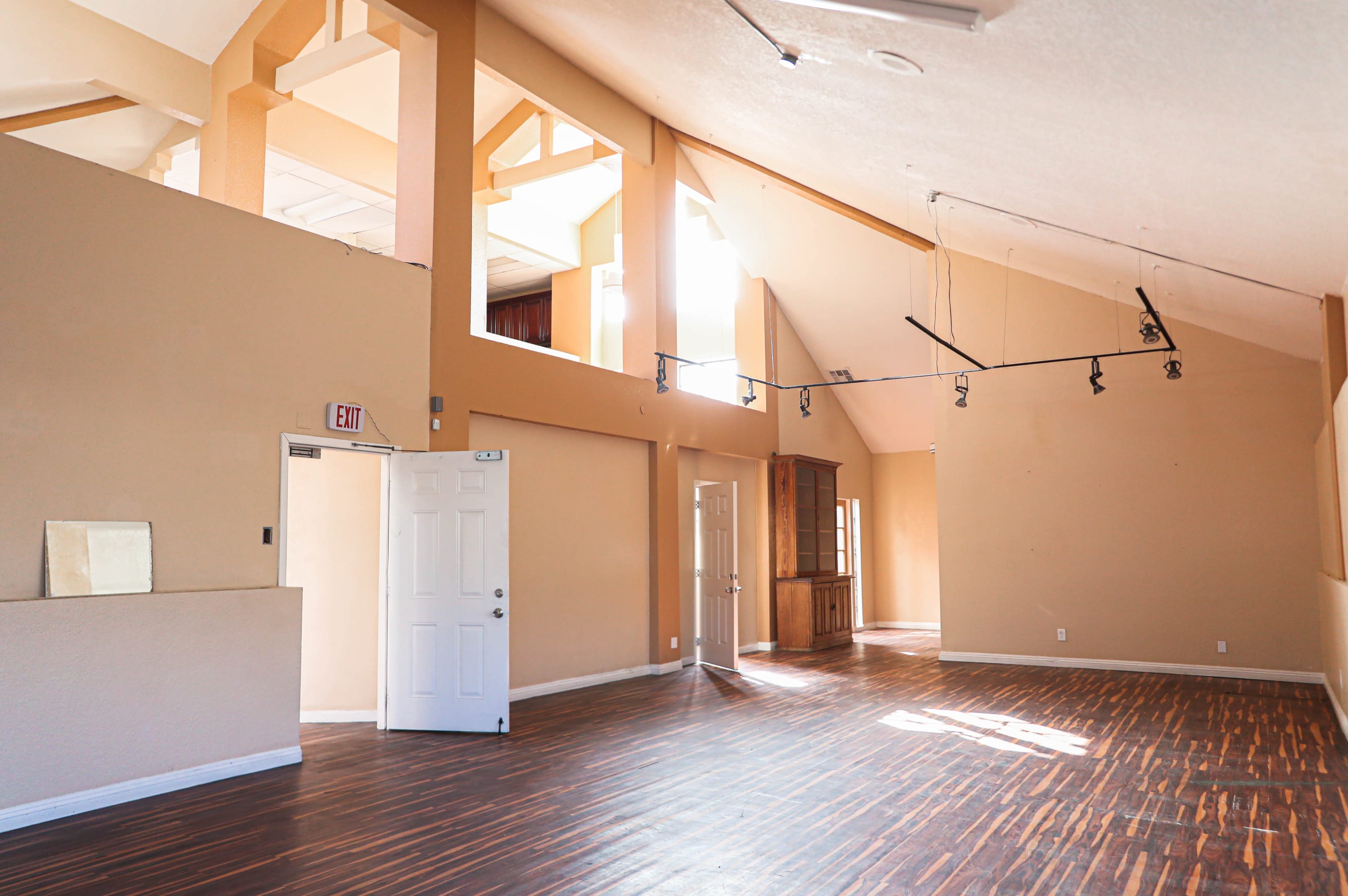 A spacious, empty room with high ceilings, large windows, and wooden flooring.
