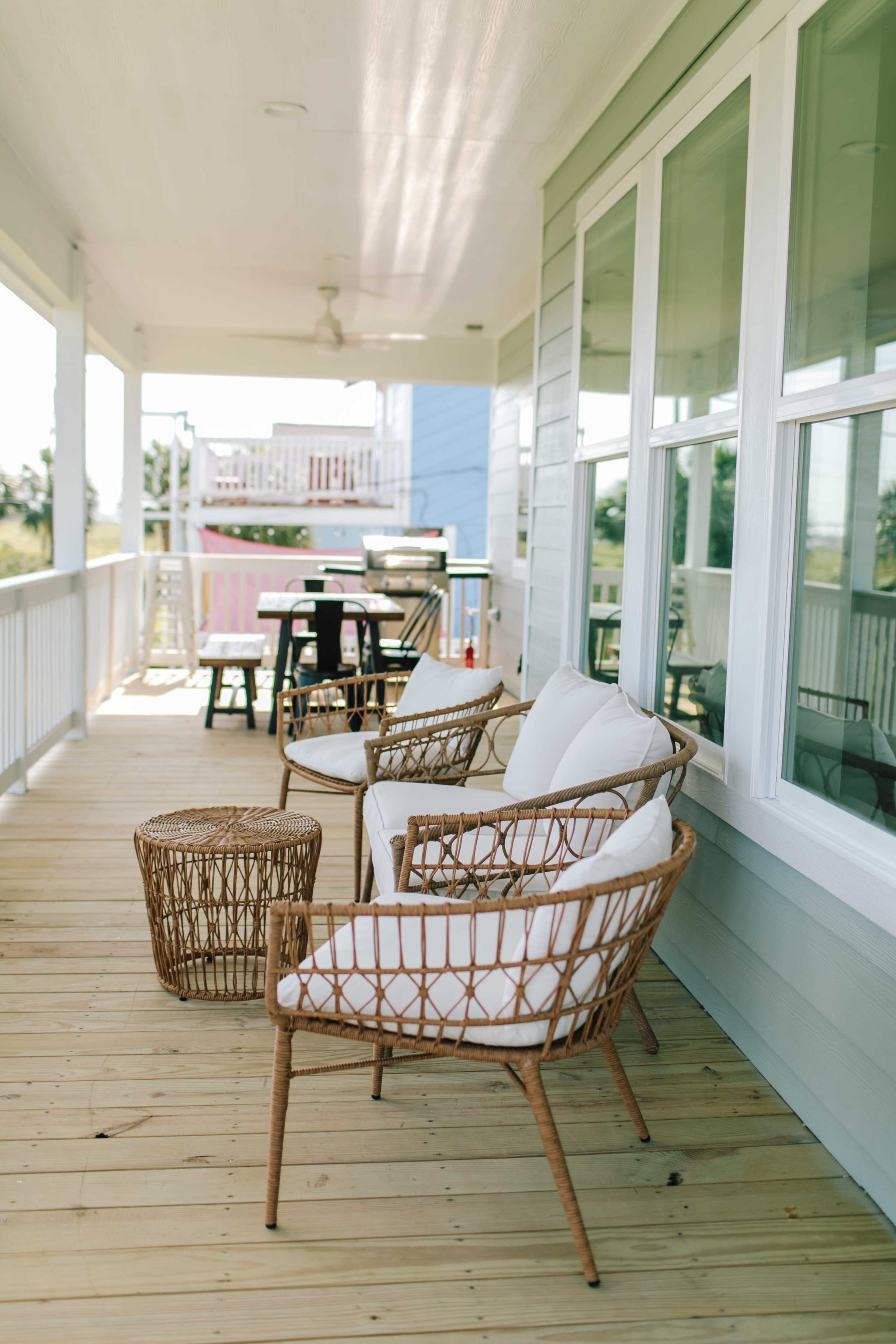 A covered porch features wicker chairs and a small table, with a dining area visible in the background.