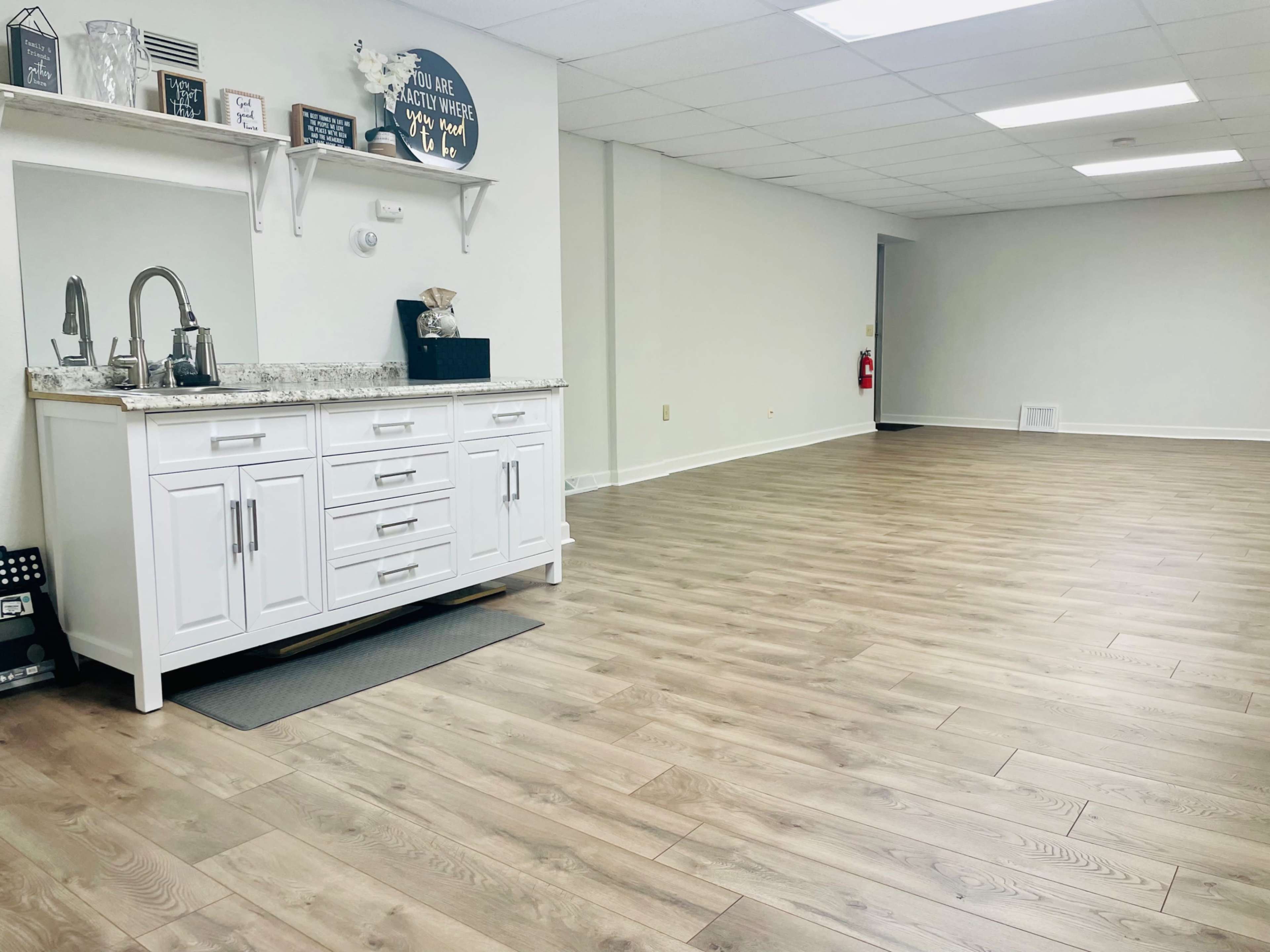 A spacious, well-lit interior featuring a white cabinet with a sink and a countertop, along with a large empty floor area.