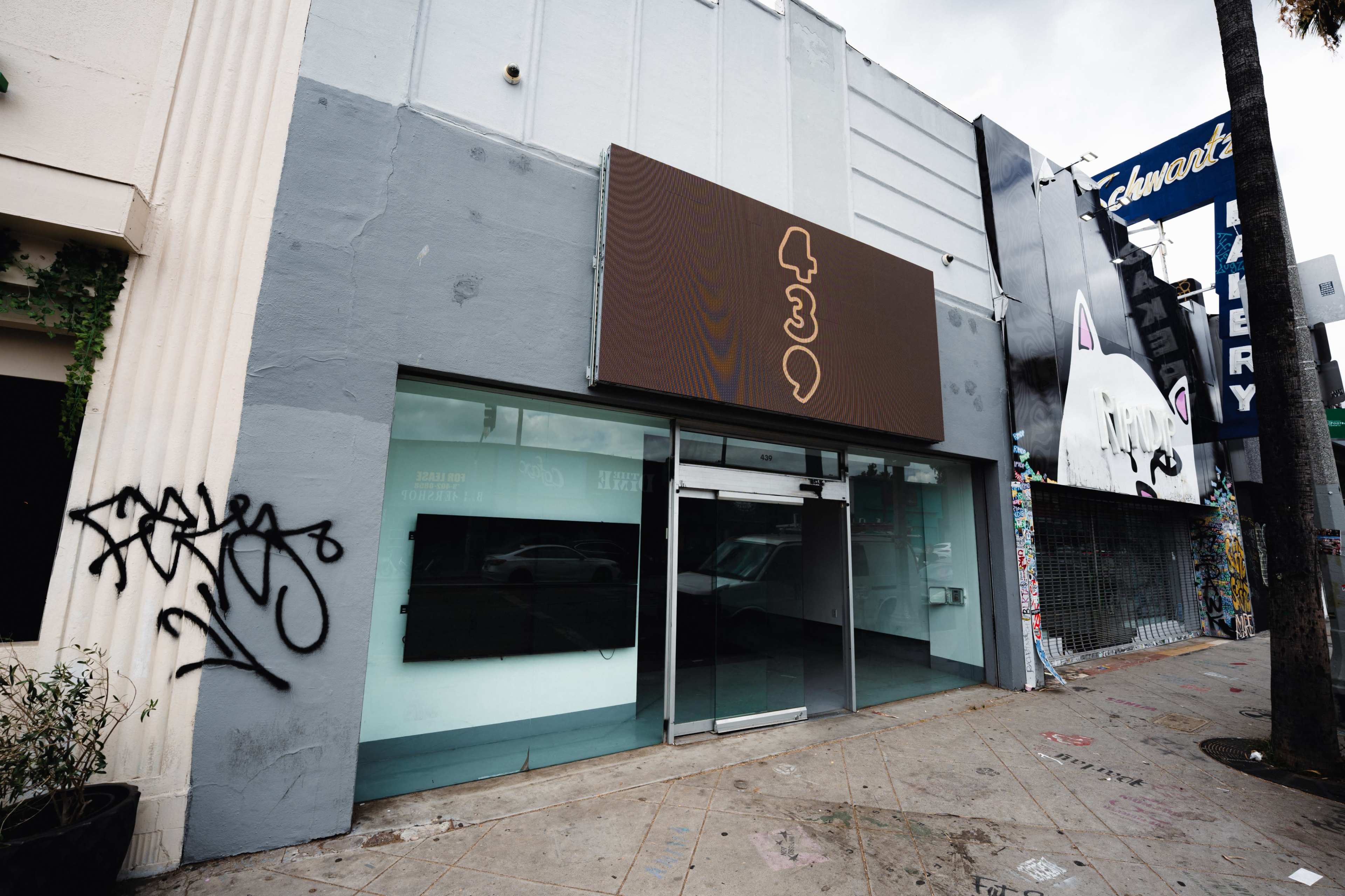 The image shows a vacant storefront with a large brown sign displaying the number "439" and graffiti on the wall nearby.