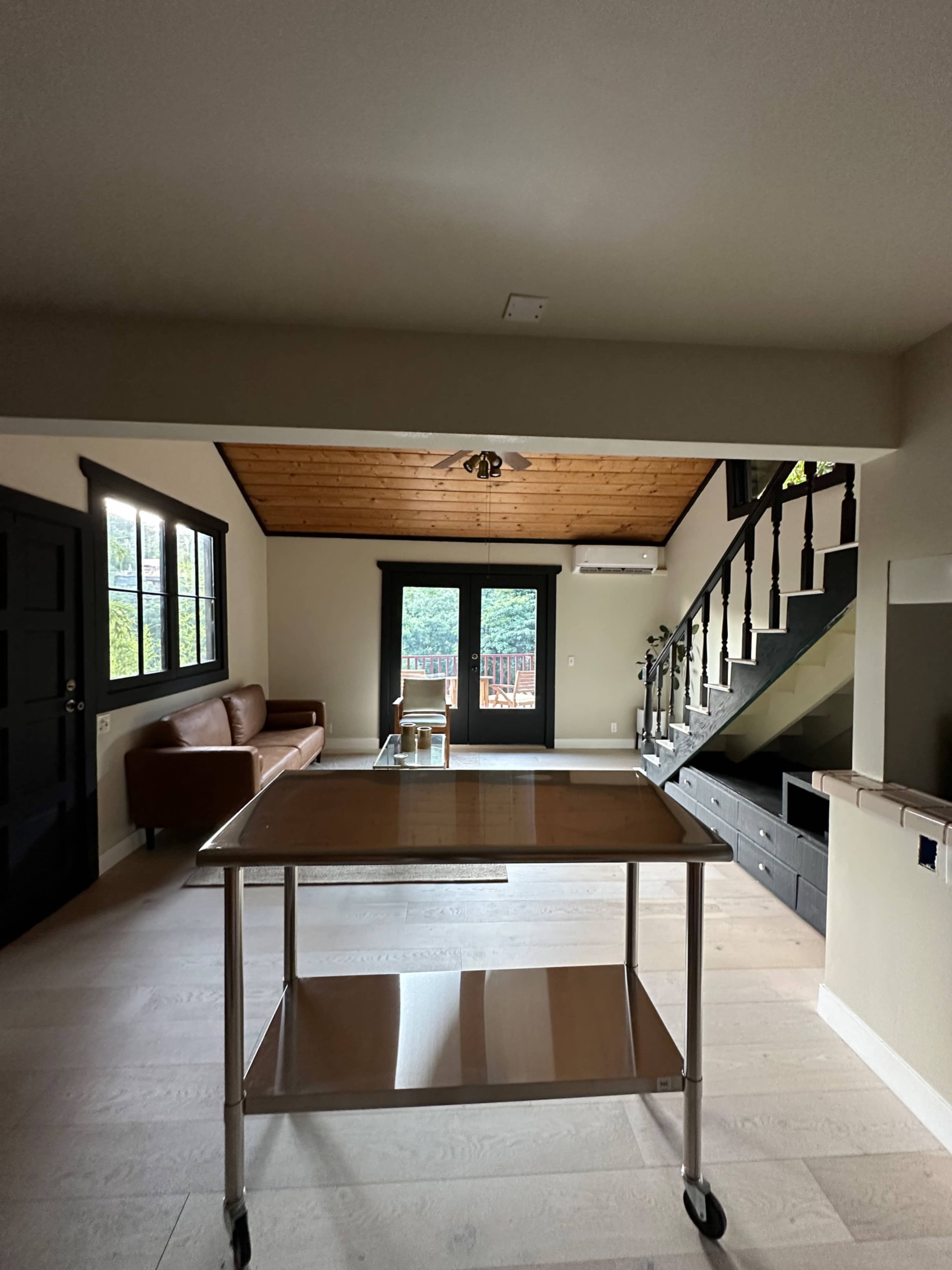A living space with a wooden ceiling, a brown leather couch, a metal cart, and a staircase leading to an upper level.