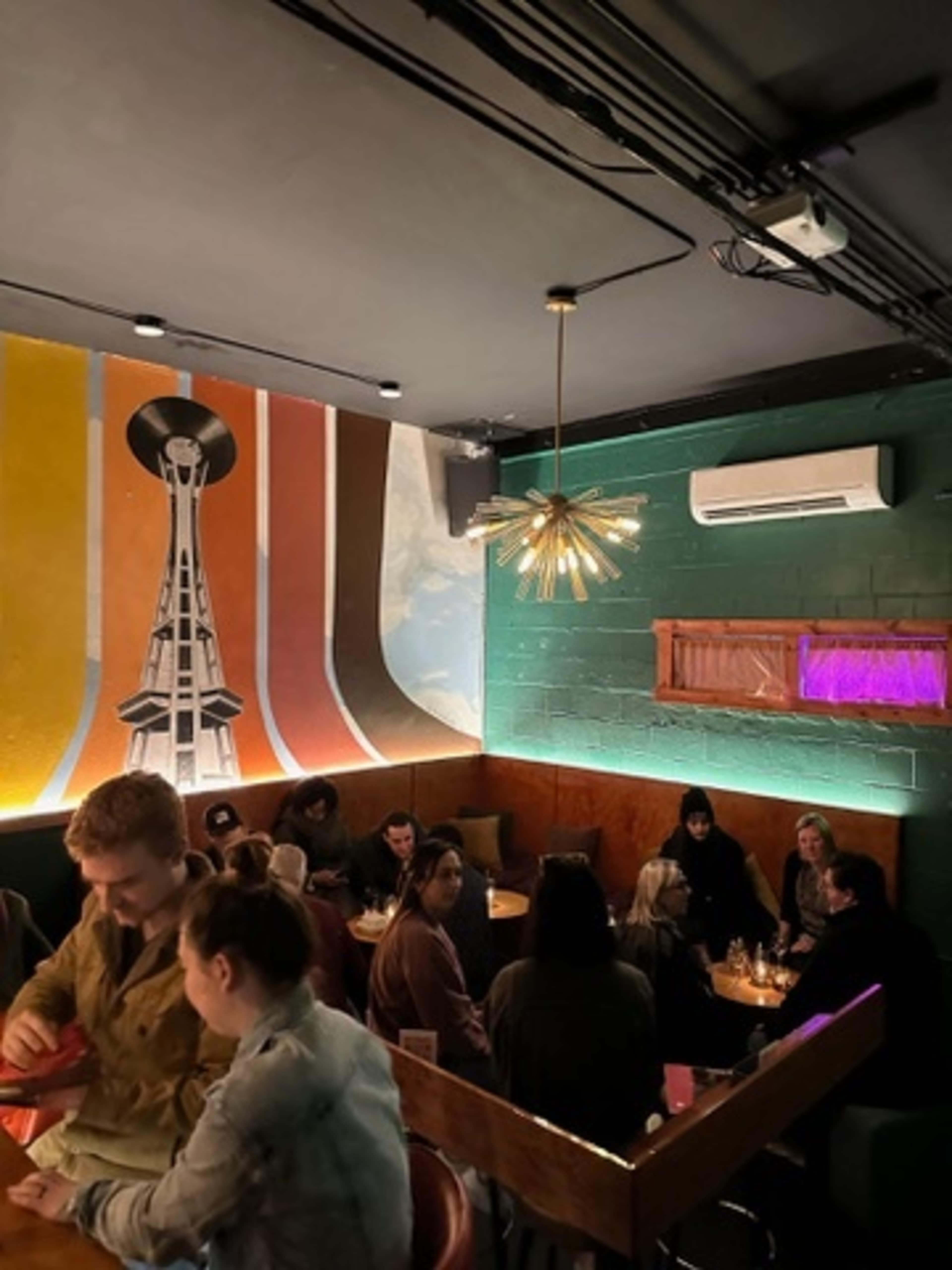 The scene depicts a lively interior of a restaurant or bar with a colorful mural and patrons seated at tables.