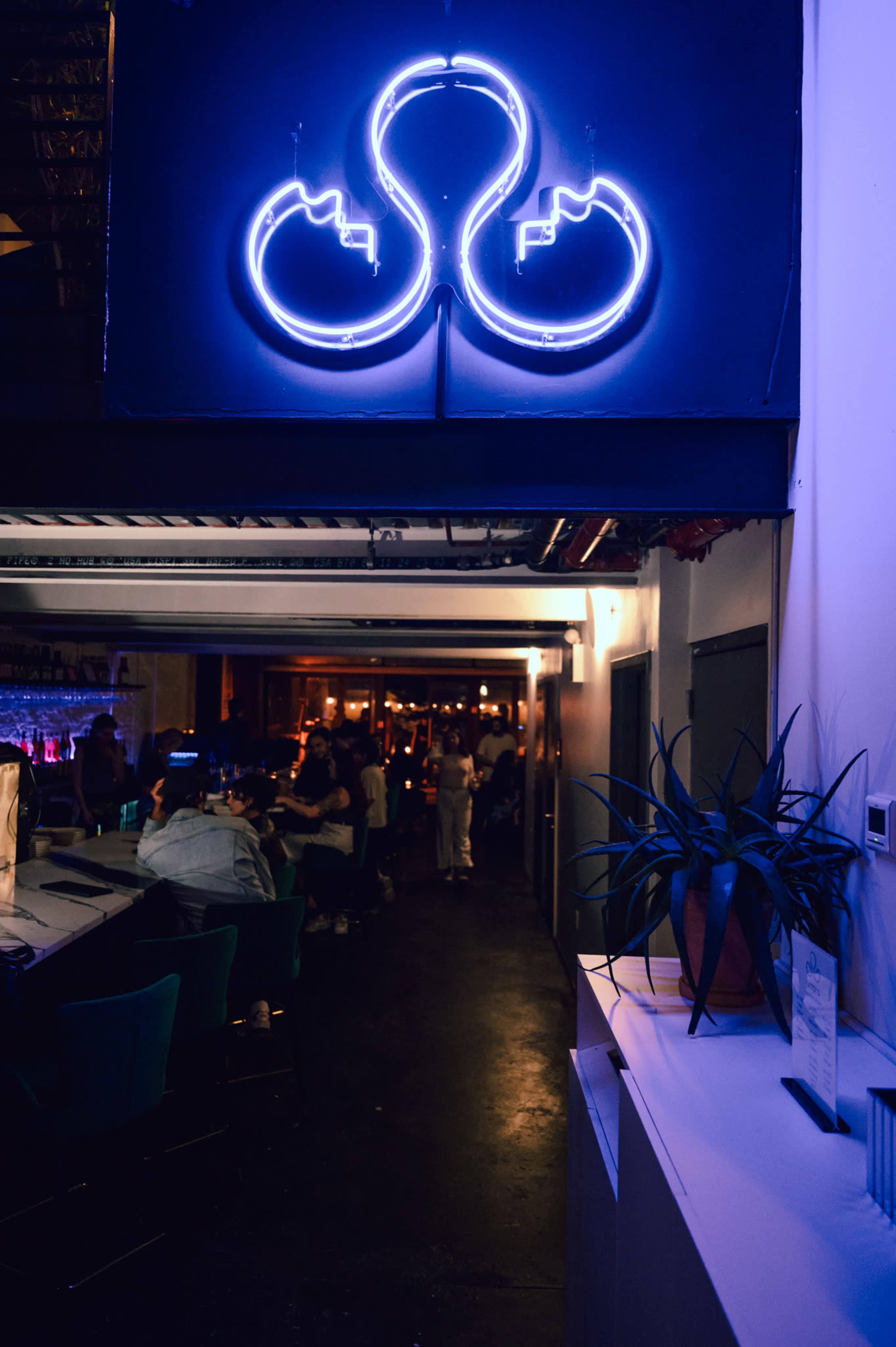 A neon sign in the shape of an octopus glows above a dimly lit bar area where patrons are gathered.