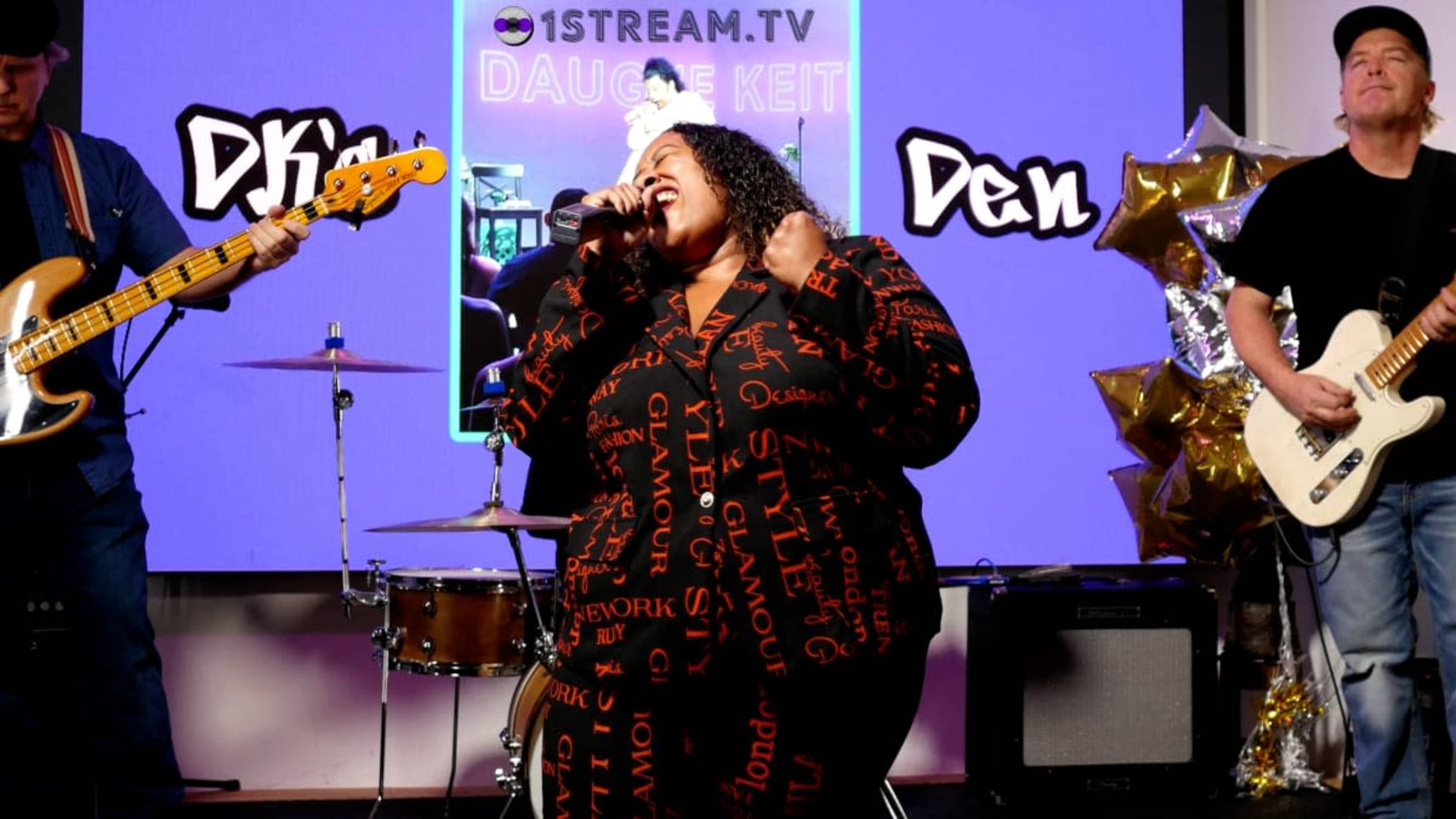 A singer performs on stage in front of a colorful backdrop while accompanied by a bassist and a guitarist.