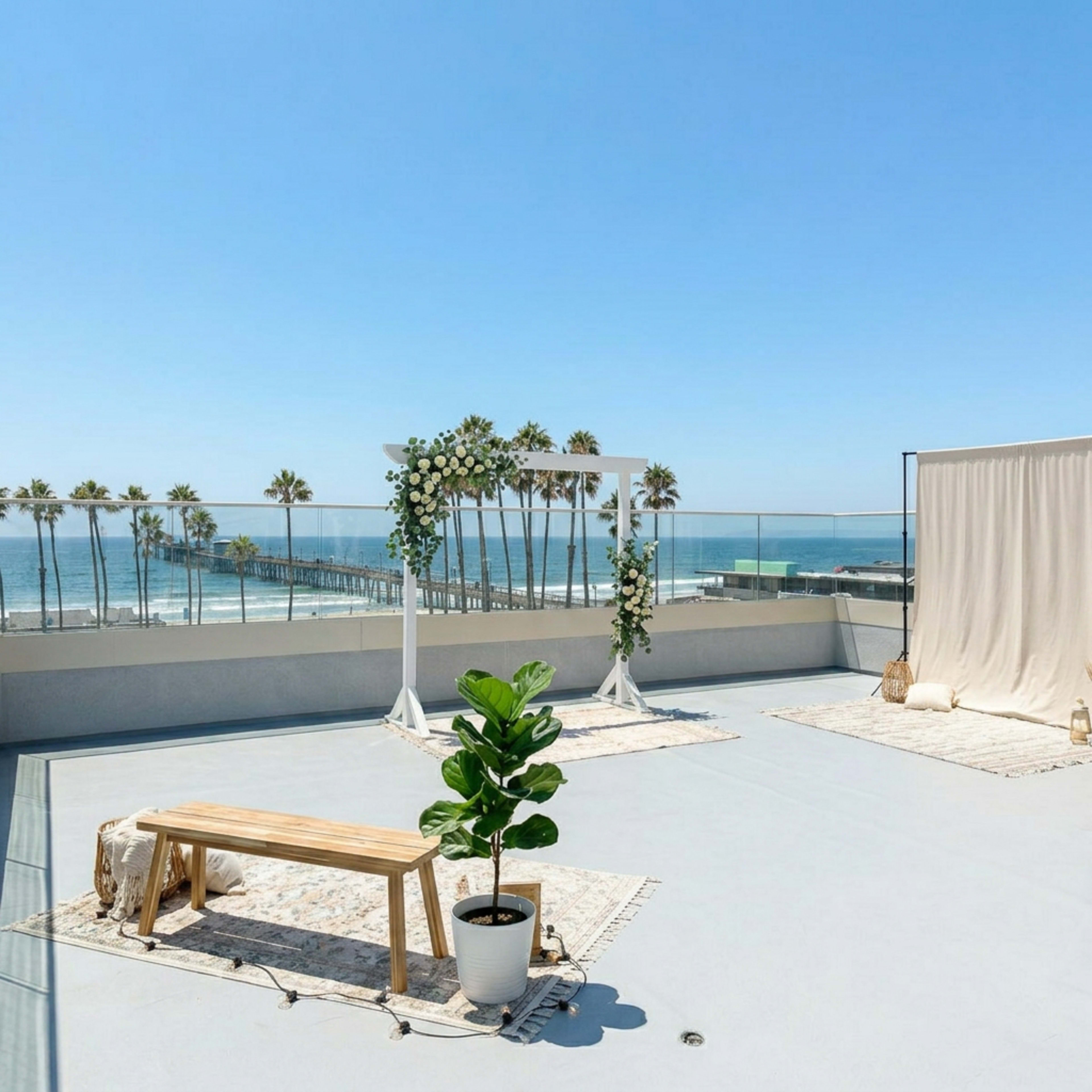 The image shows a rooftop venue with a decorative arch and seating area overlooking a pier and ocean in clear weather.