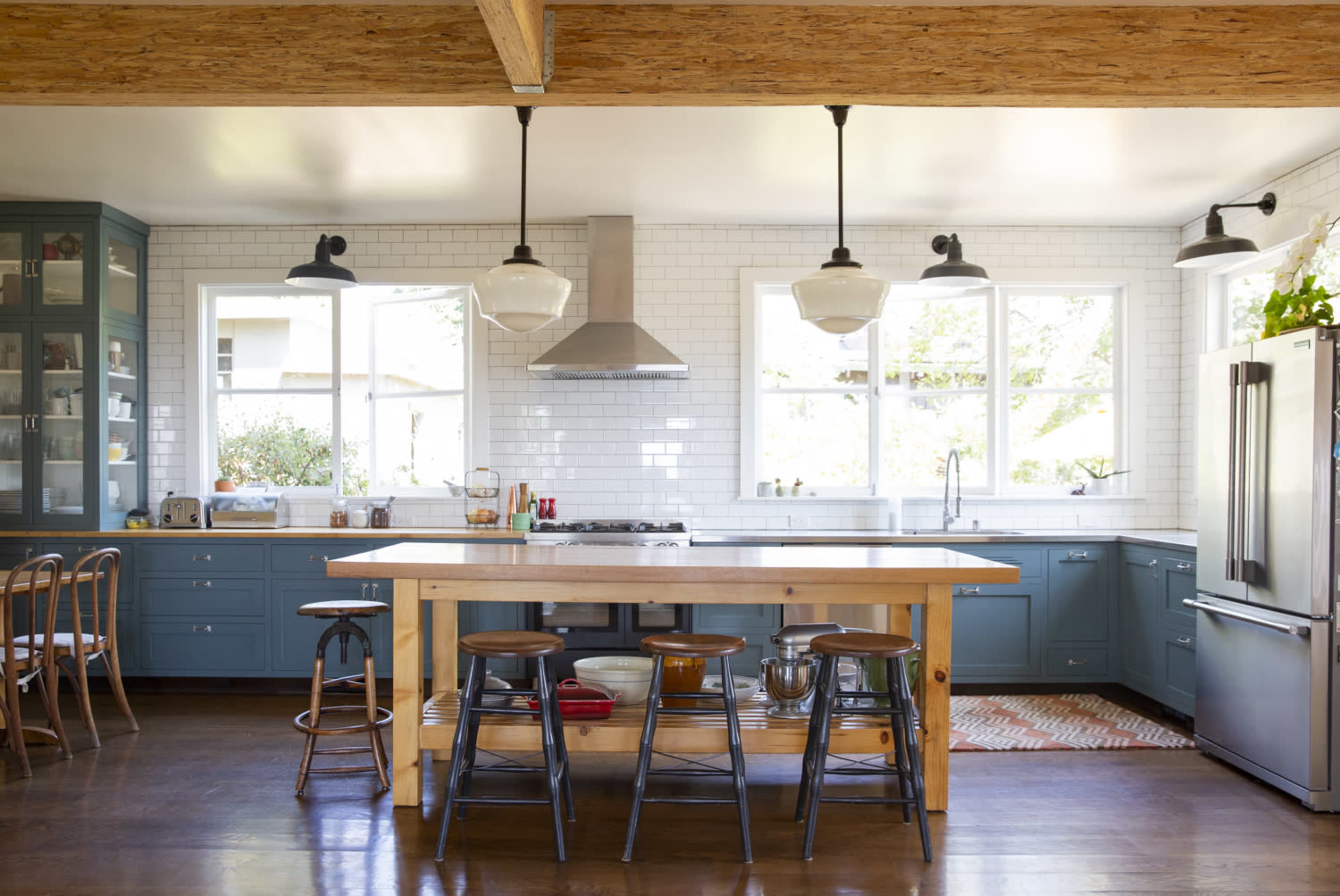 A spacious kitchen features blue cabinetry, a wooden island with stools, and large windows that allow natural light to enter.