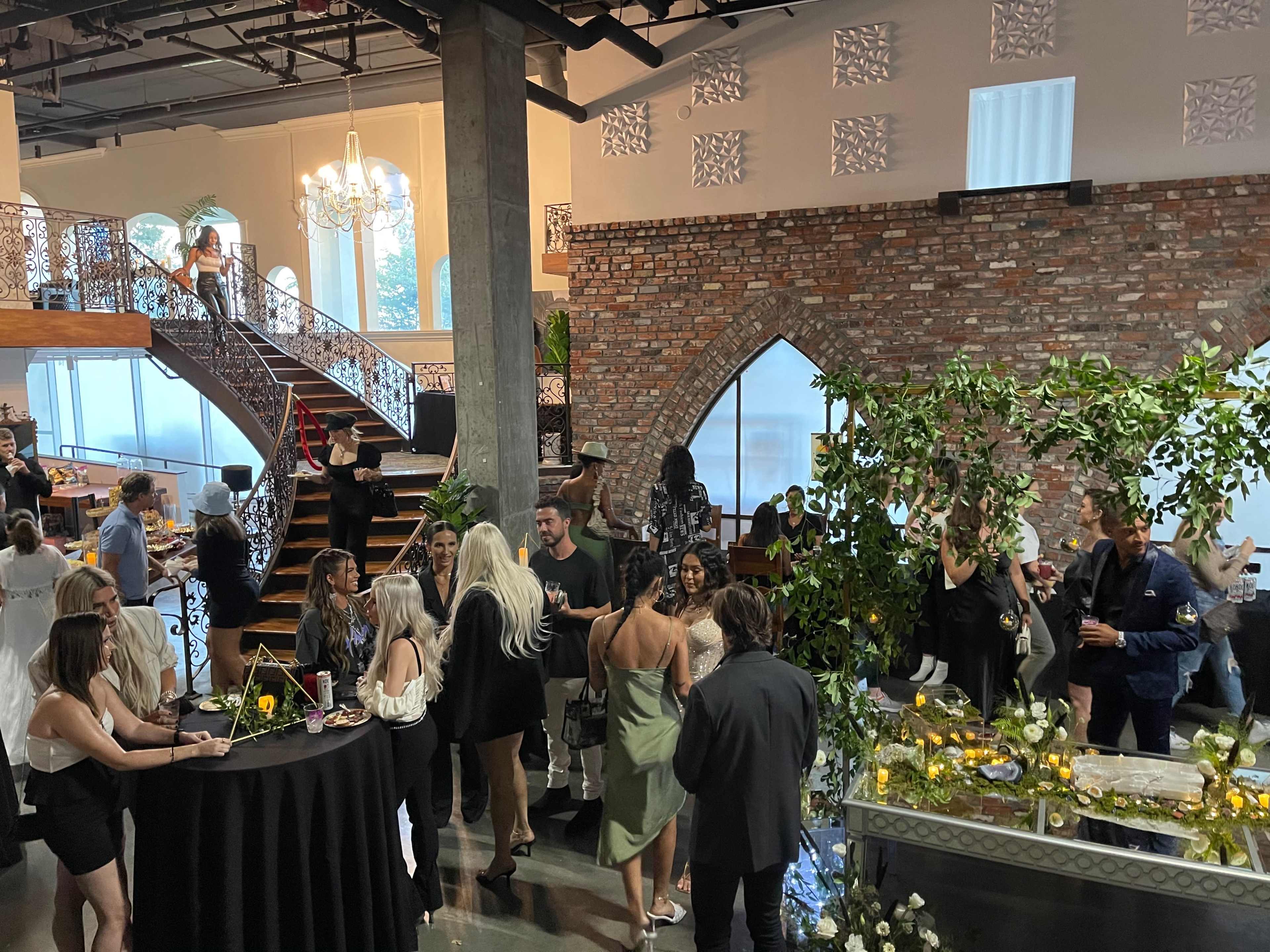 A group of people socializes at a stylish event held in a modern venue with exposed brick walls and elegant architecture.
