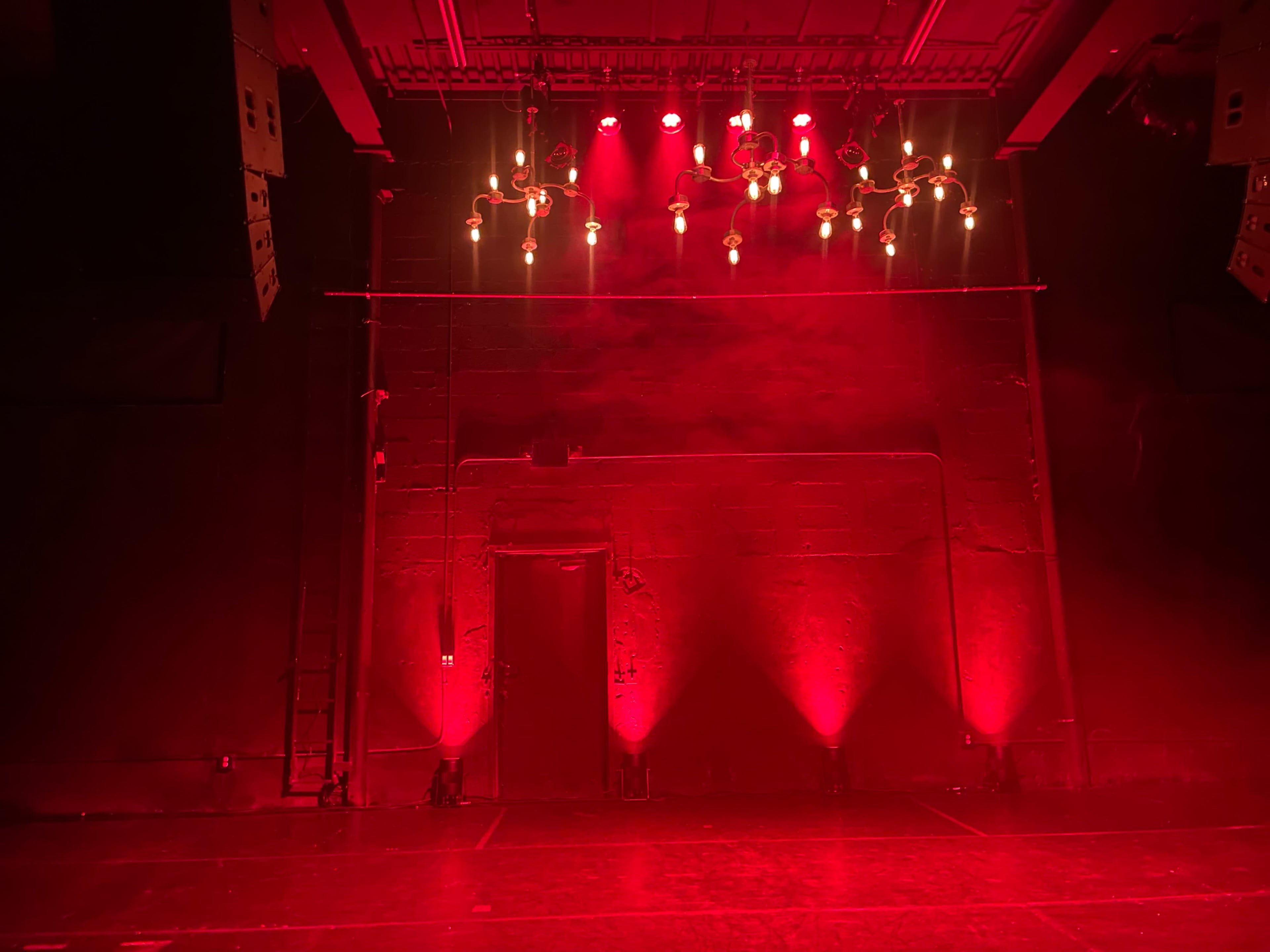 The scene features a stage illuminated by red lights, with a chandelier overhead and an unlit doorway on the left side.
