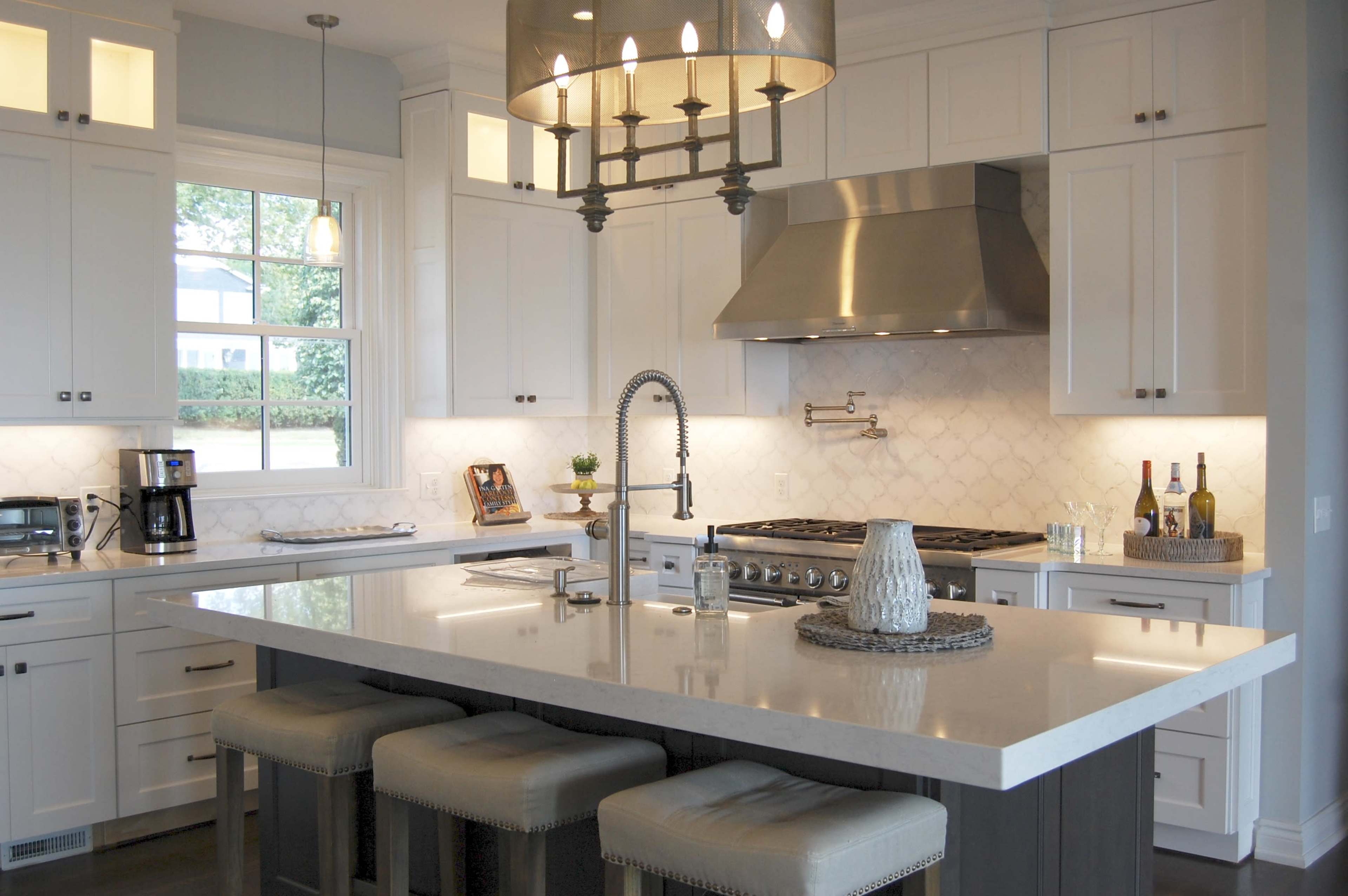 A modern kitchen featuring white cabinetry, a large central island with bar stools, stainless steel appliances, and a chandelier above the island.