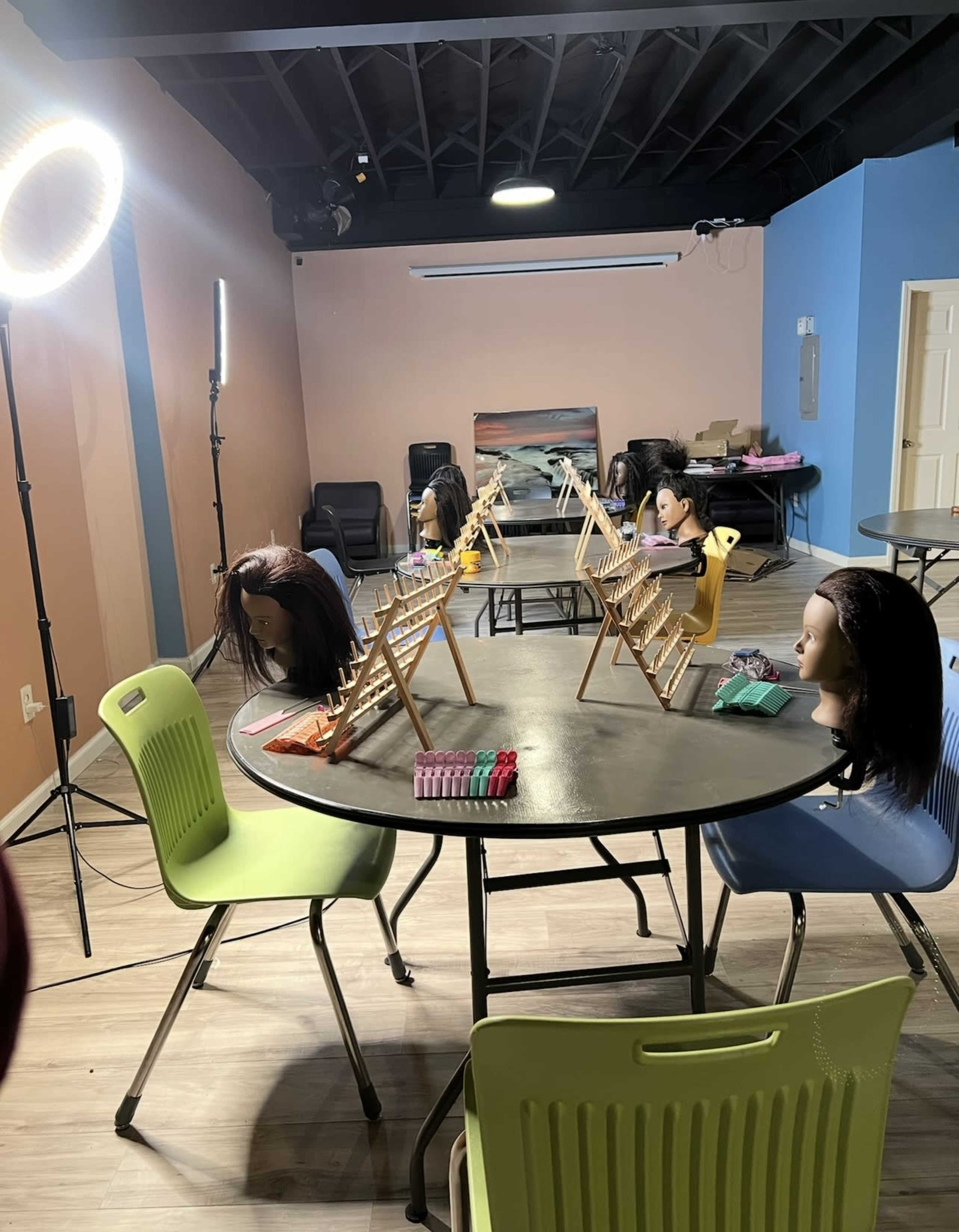The image shows a room set up for hair styling practice, with multiple mannequin heads on tables, surrounded by styling tools and equipment.