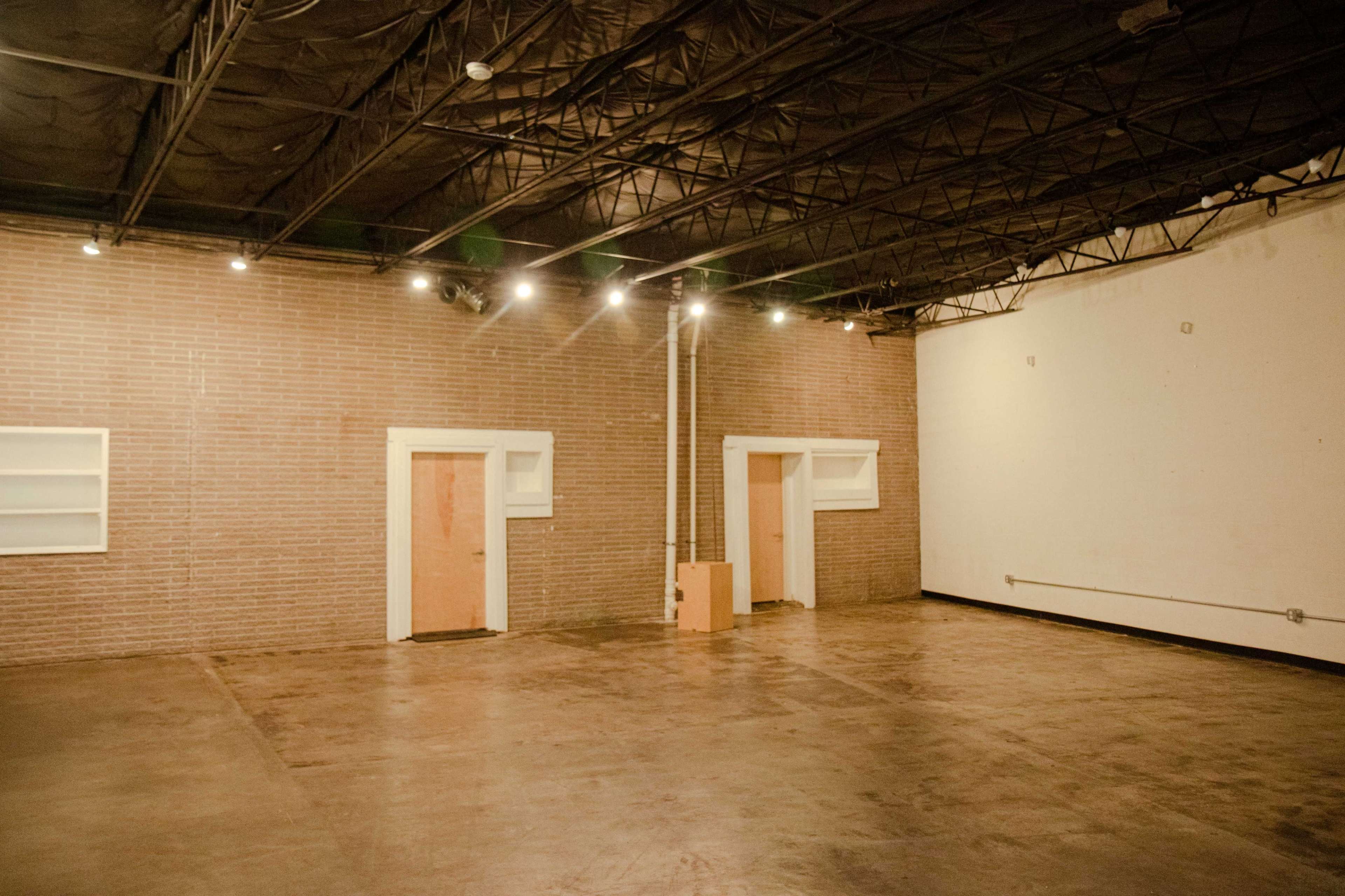 An empty industrial space with exposed brick walls and two closed doors on the left side.