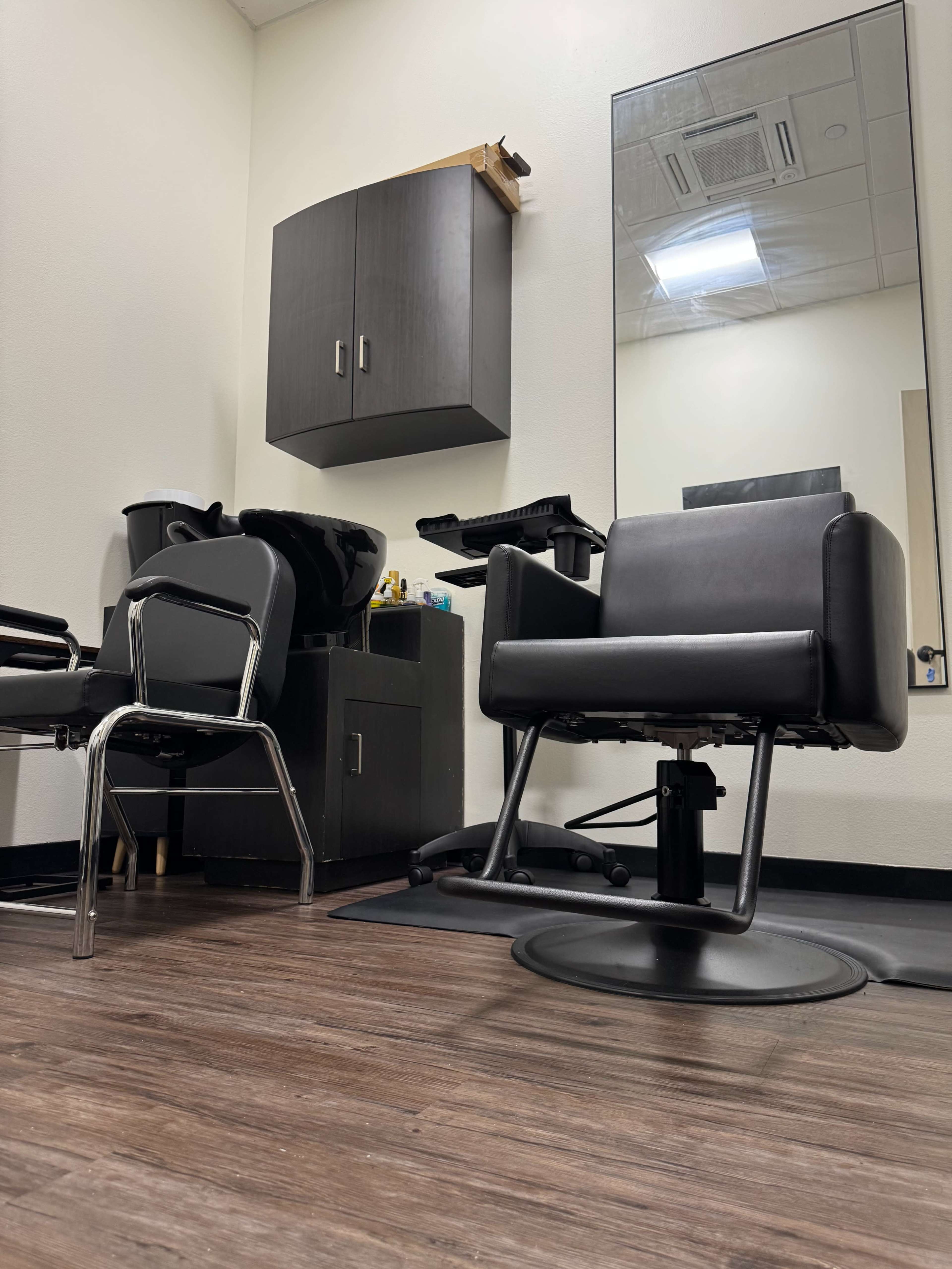 The image shows a hair salon interior with a stylist's chair, a shampoo basin, and a large mirror mounted on the wall.