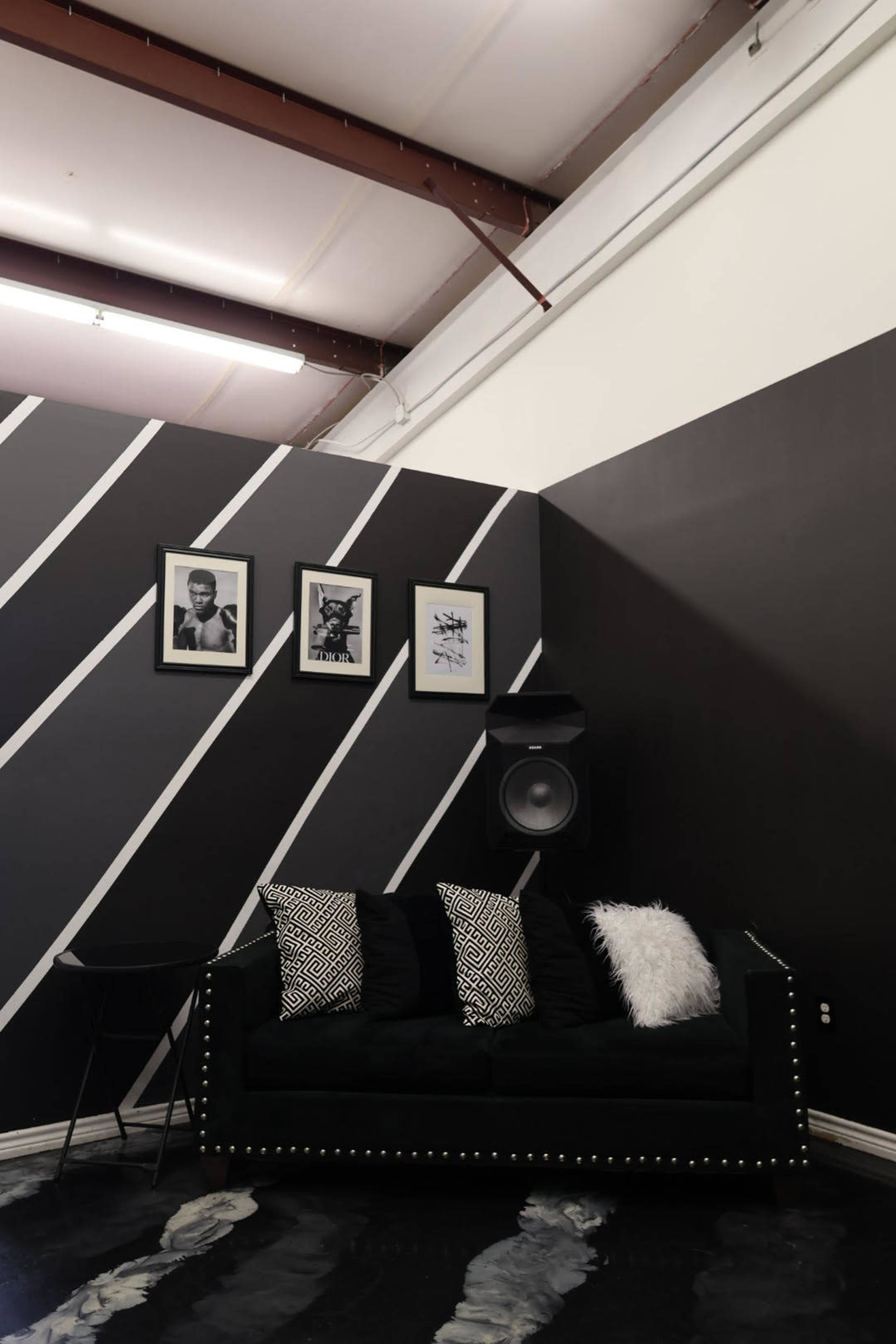 The image shows a black and white-themed lounge area with a black sofa, decorative cushions, and framed artwork on the wall.