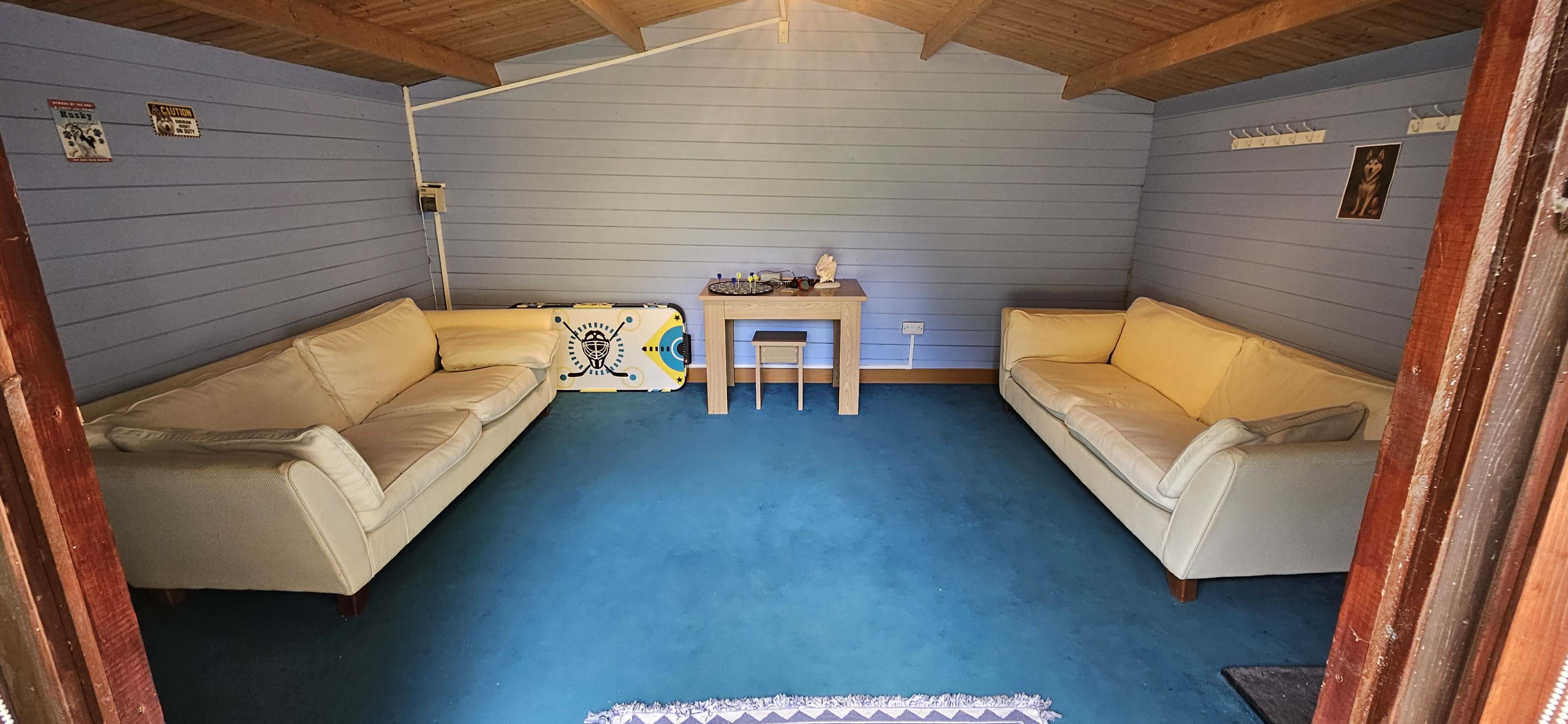 The image shows a small, neatly organized room with two white couches facing each other and a wooden table in the center, set on a blue carpeted floor.