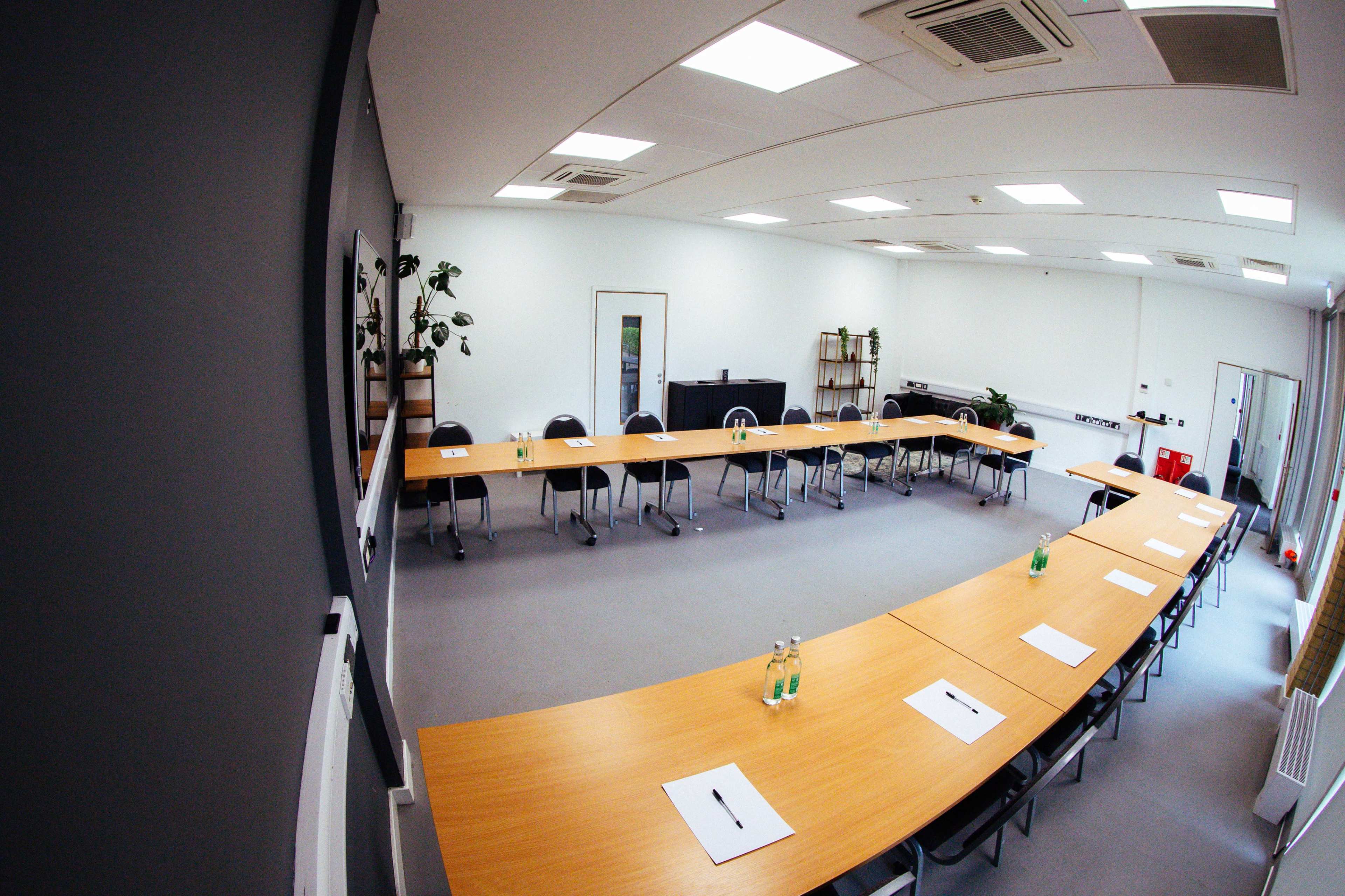 The image shows a conference room with a large rectangular table, chairs arranged around it, and minimal decorations.