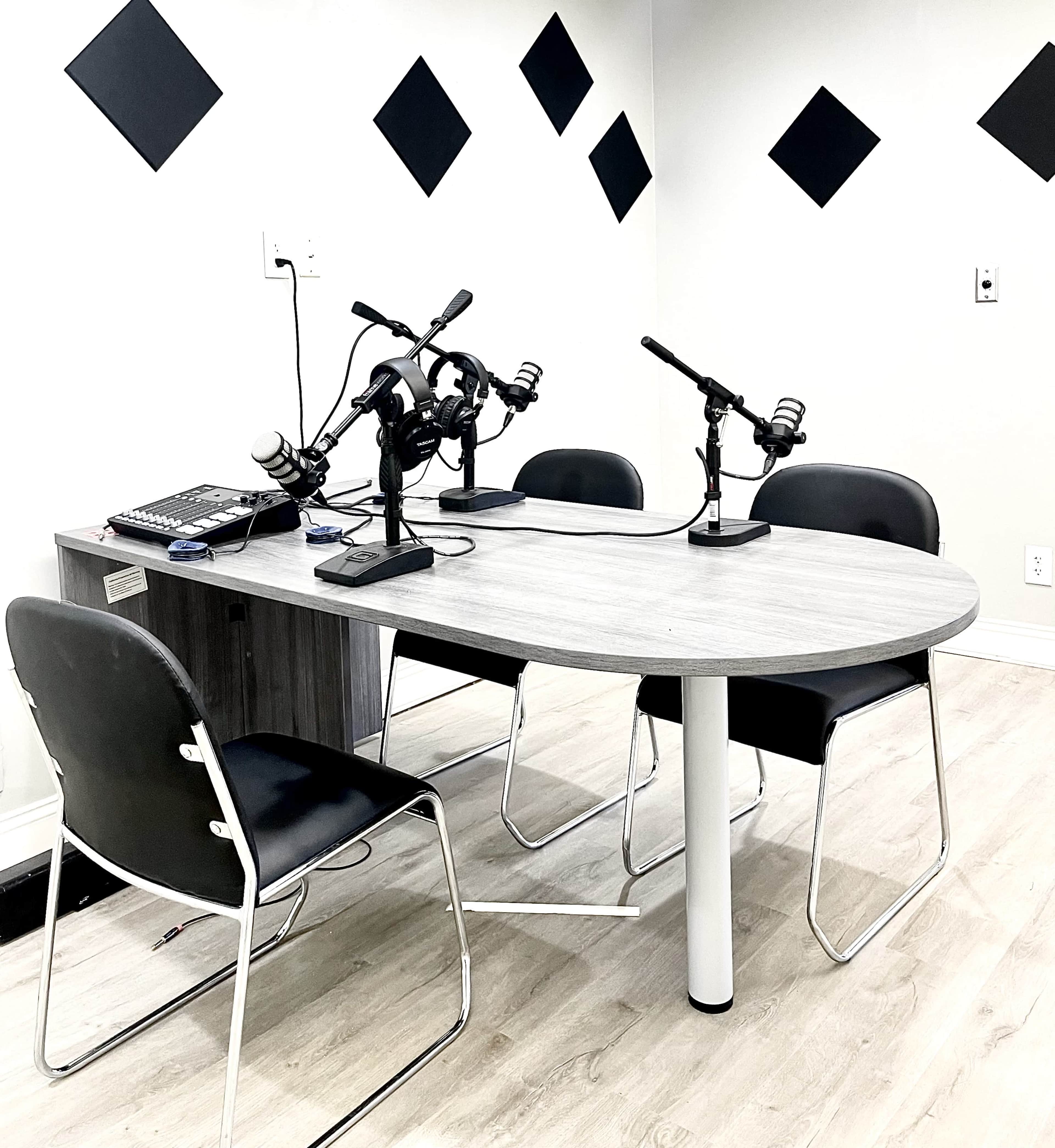 A modern podcast studio with a table, four chairs, and three microphones set up on the table.