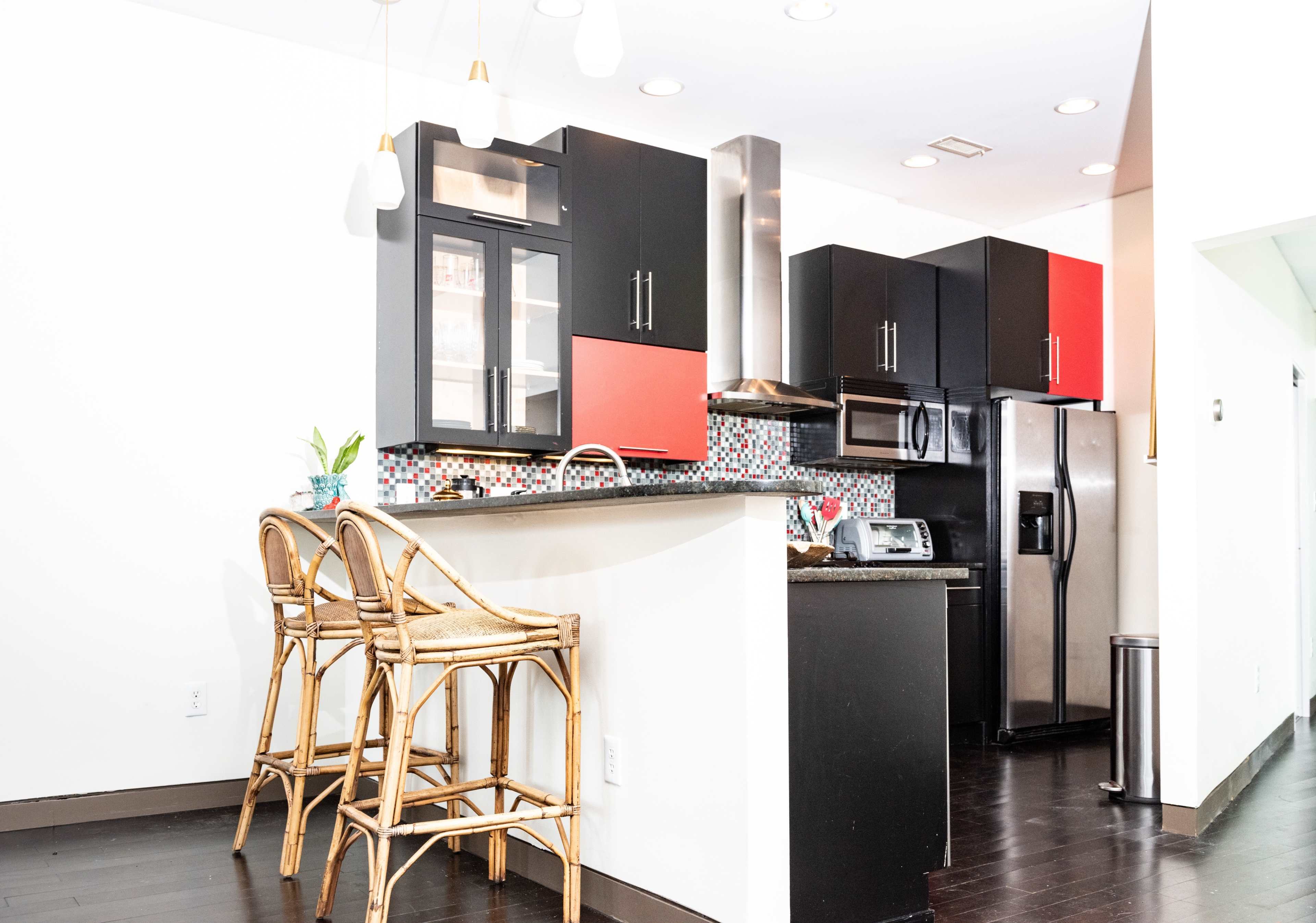 A modern kitchen with black and red cabinetry, a bar area with three rattan stools, and stainless steel appliances.