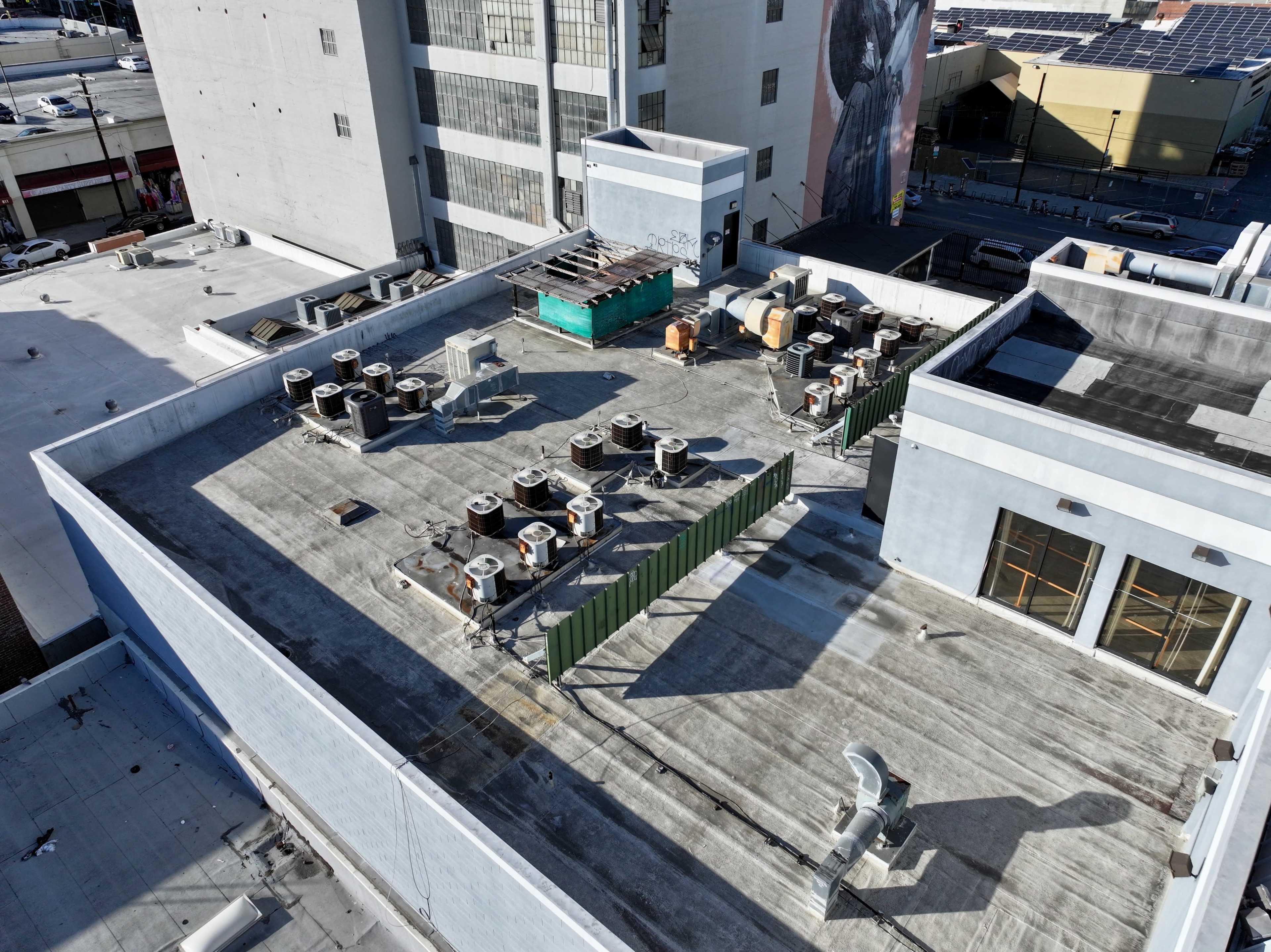 The rooftop of a building featuring multiple air conditioning units, a green barrier, and various construction materials scattered across the surface.