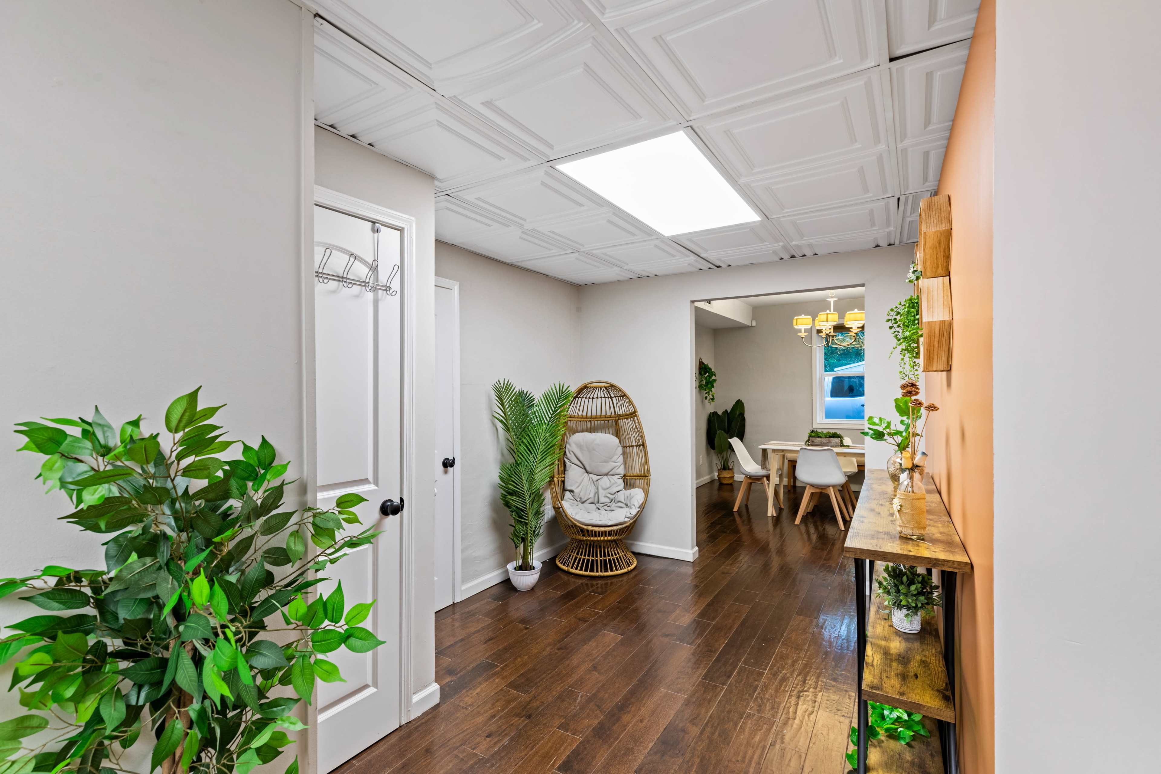 A hallway leads to a dining area with a table and chairs, featuring an indoor plant and a decorative wall shelf.