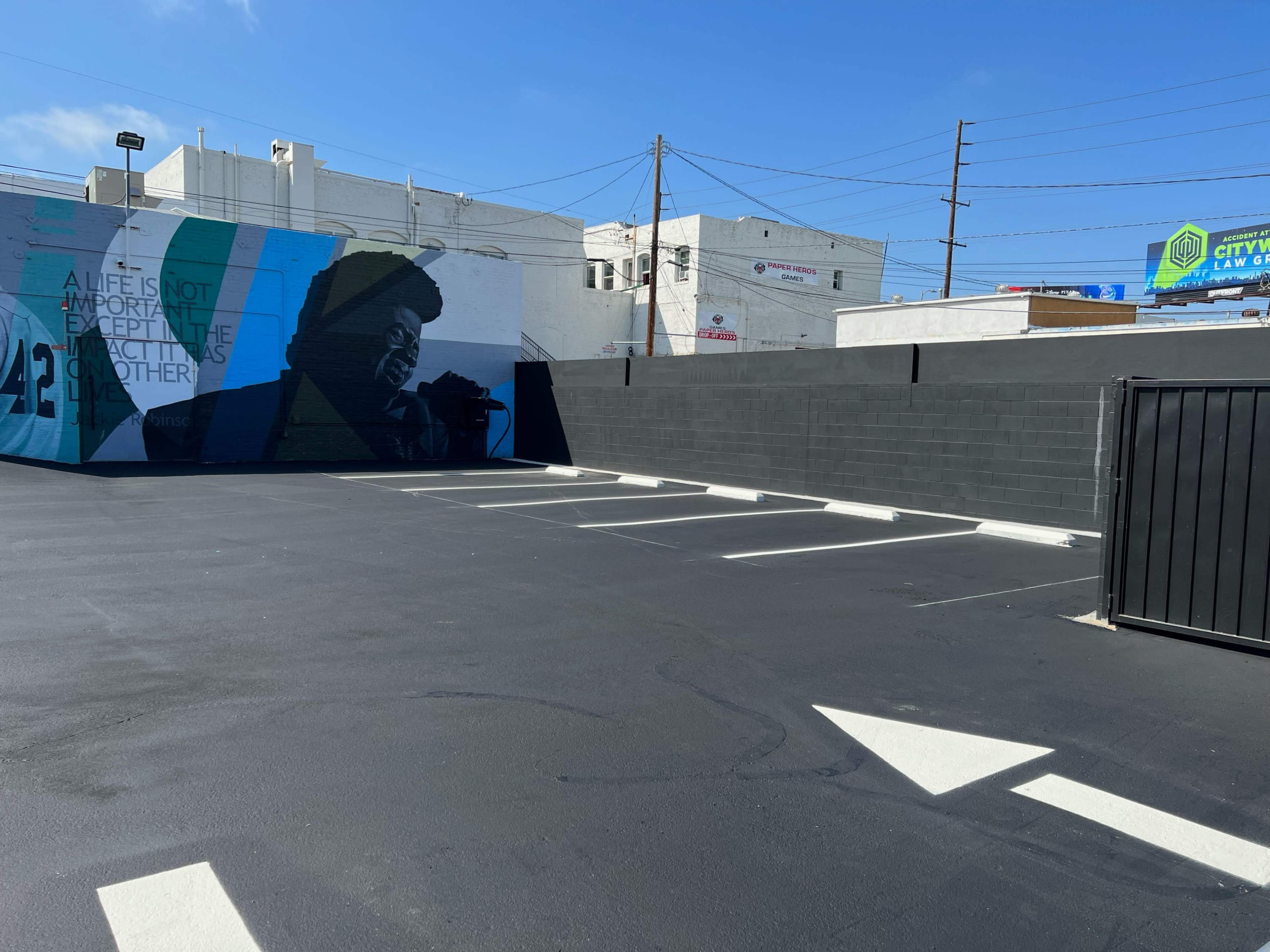 A parking lot with freshly painted white lines, featuring a mural of a person on a nearby wall and a black fence dividing the area.