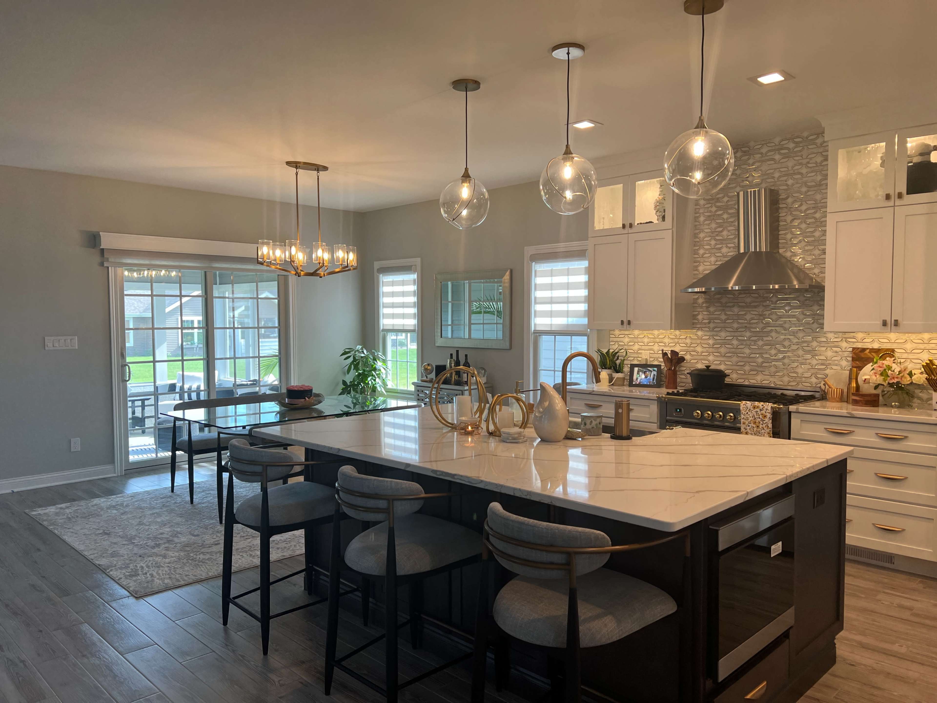 A modern kitchen features a large island with seating, pendant lighting, white cabinets, and a dining area with sliding glass doors leading to an outdoor space.