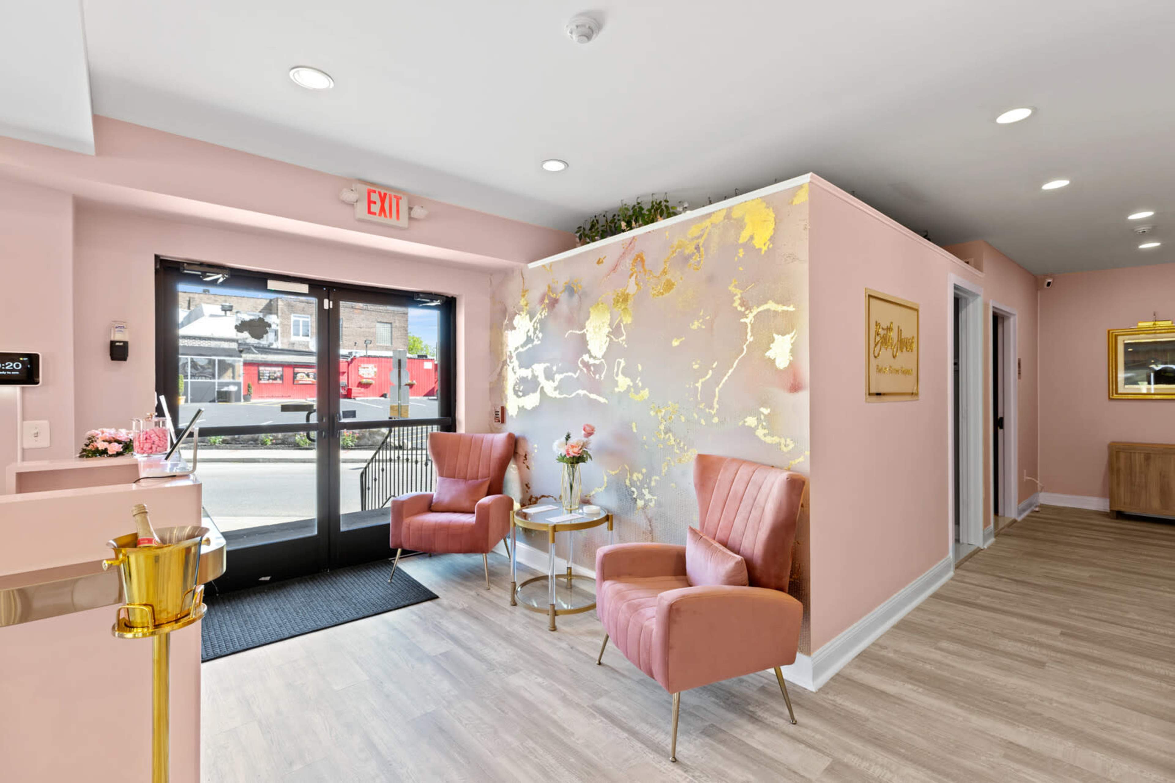 A modern reception area with pink walls, two pink chairs, and a decorative gold accent wall near the entrance.