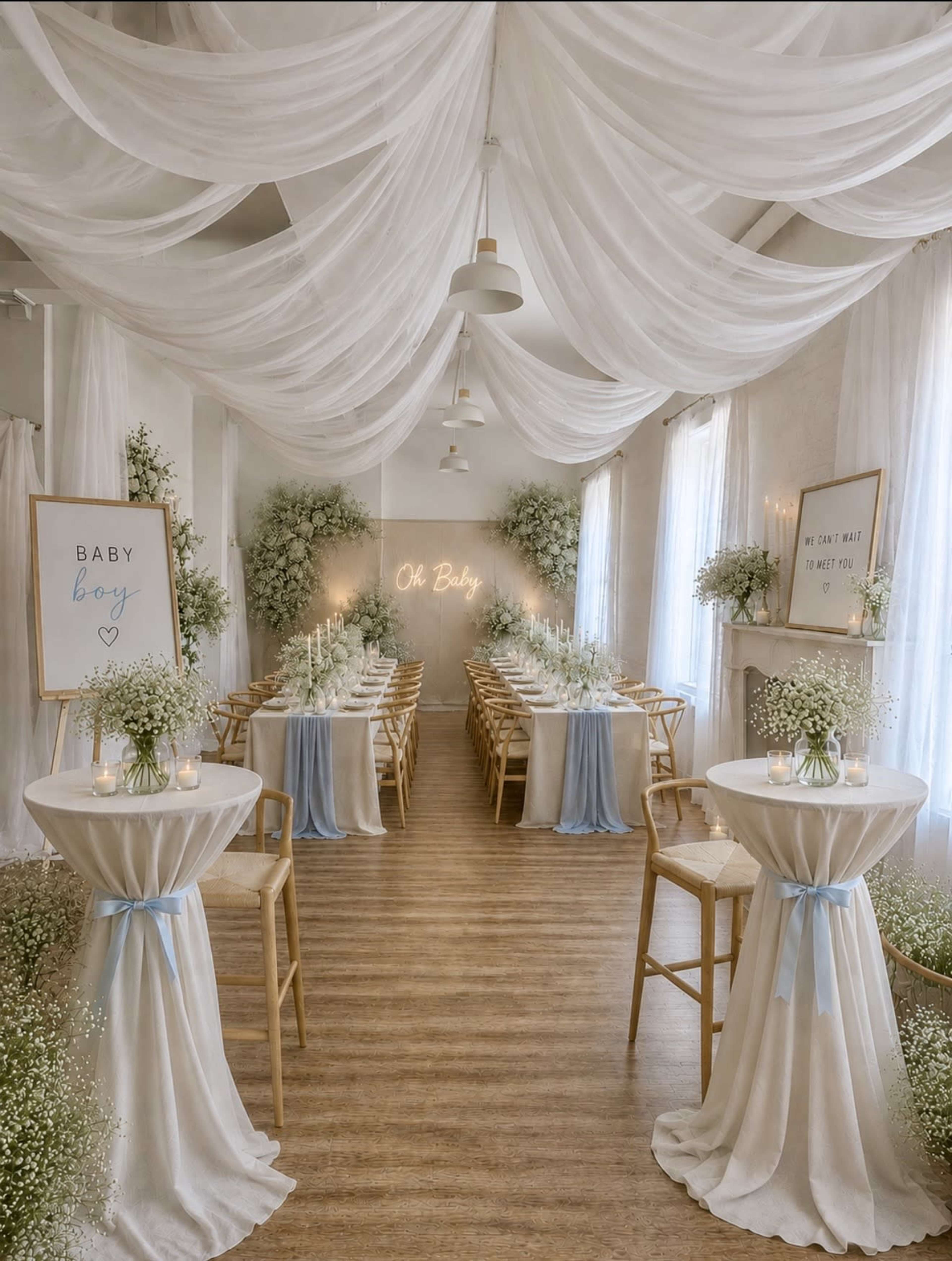 The image shows a decorated event space for a baby shower, featuring tables draped in white cloth, floral arrangements, and soft lighting.