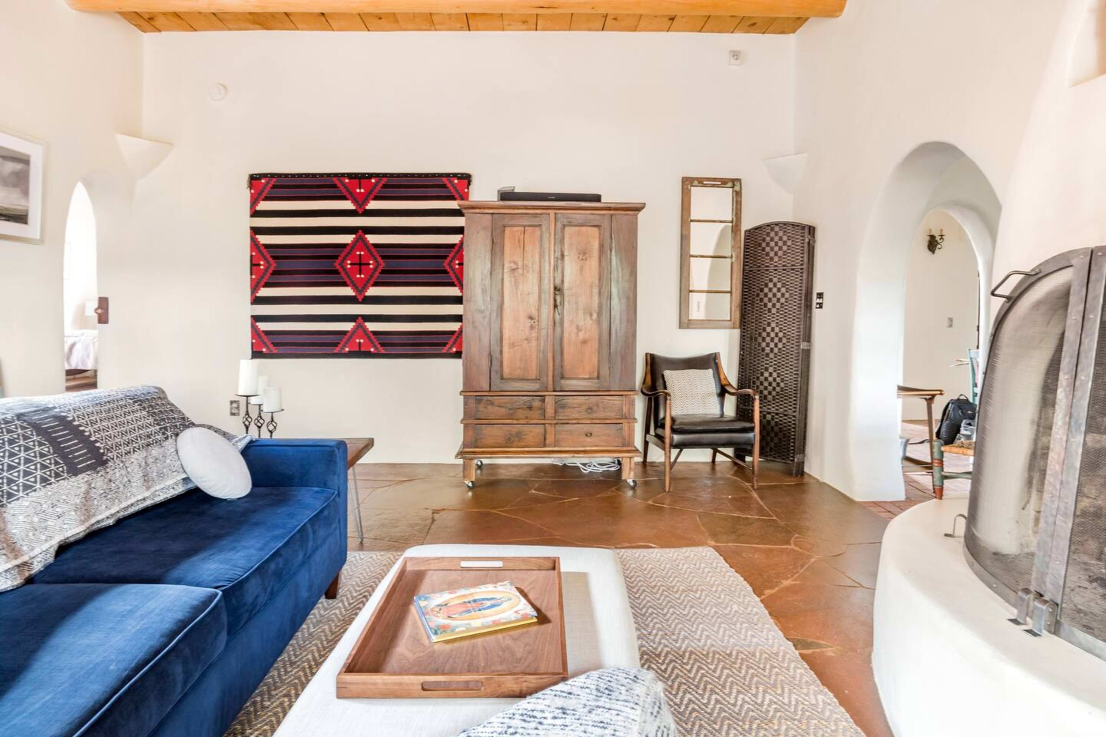 A well-furnished living room with a blue sofa, a wooden wardrobe, and a textured rug on a tile floor.
