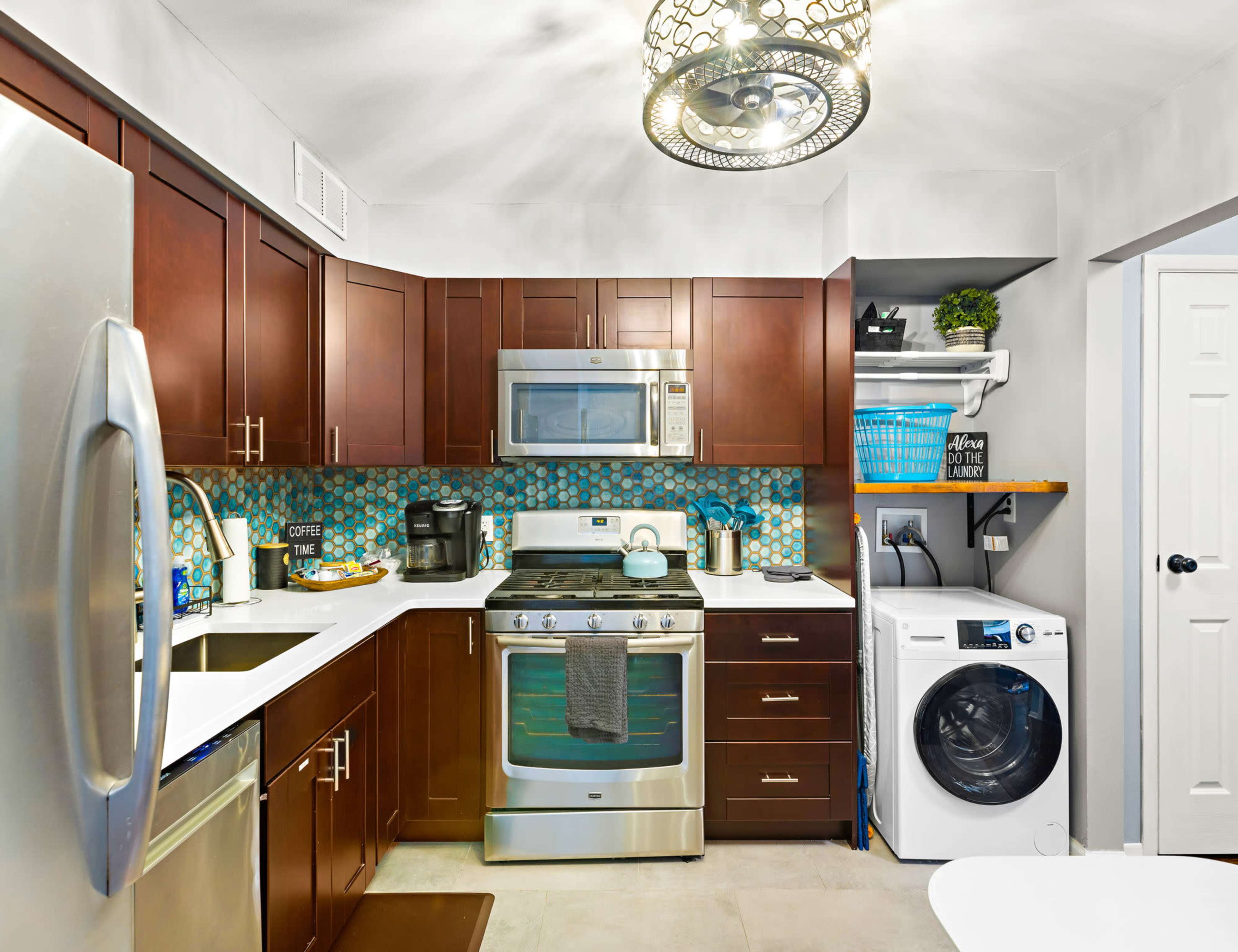 A modern kitchen features dark wood cabinets, stainless steel appliances, a tile backsplash, and a washer and dryer integrated into the cabinetry.