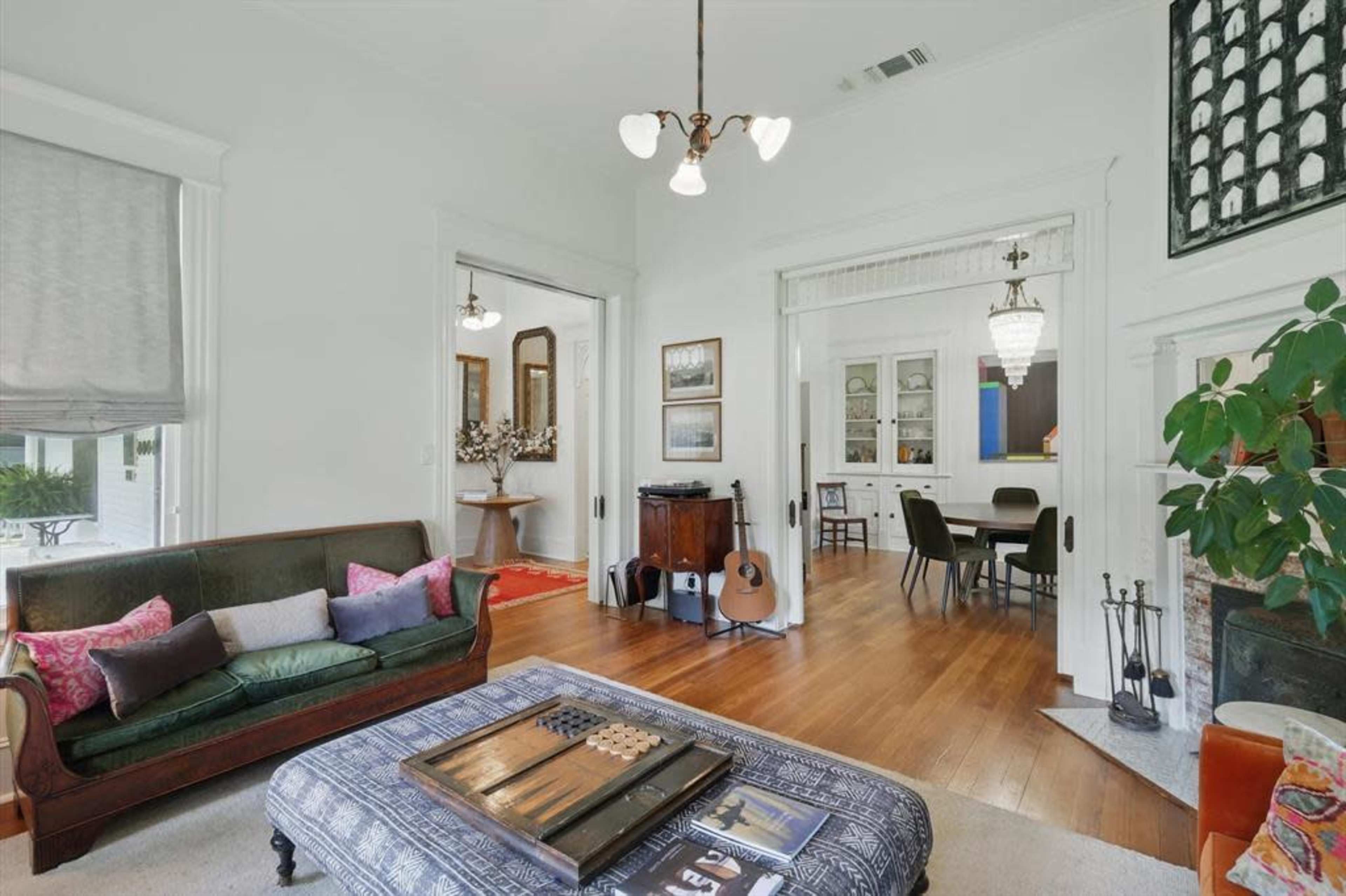The image shows a living room with a green sofa, a coffee table with a decorative cloth, and a view into a dining area featuring a round table and modern lighting fixtures.