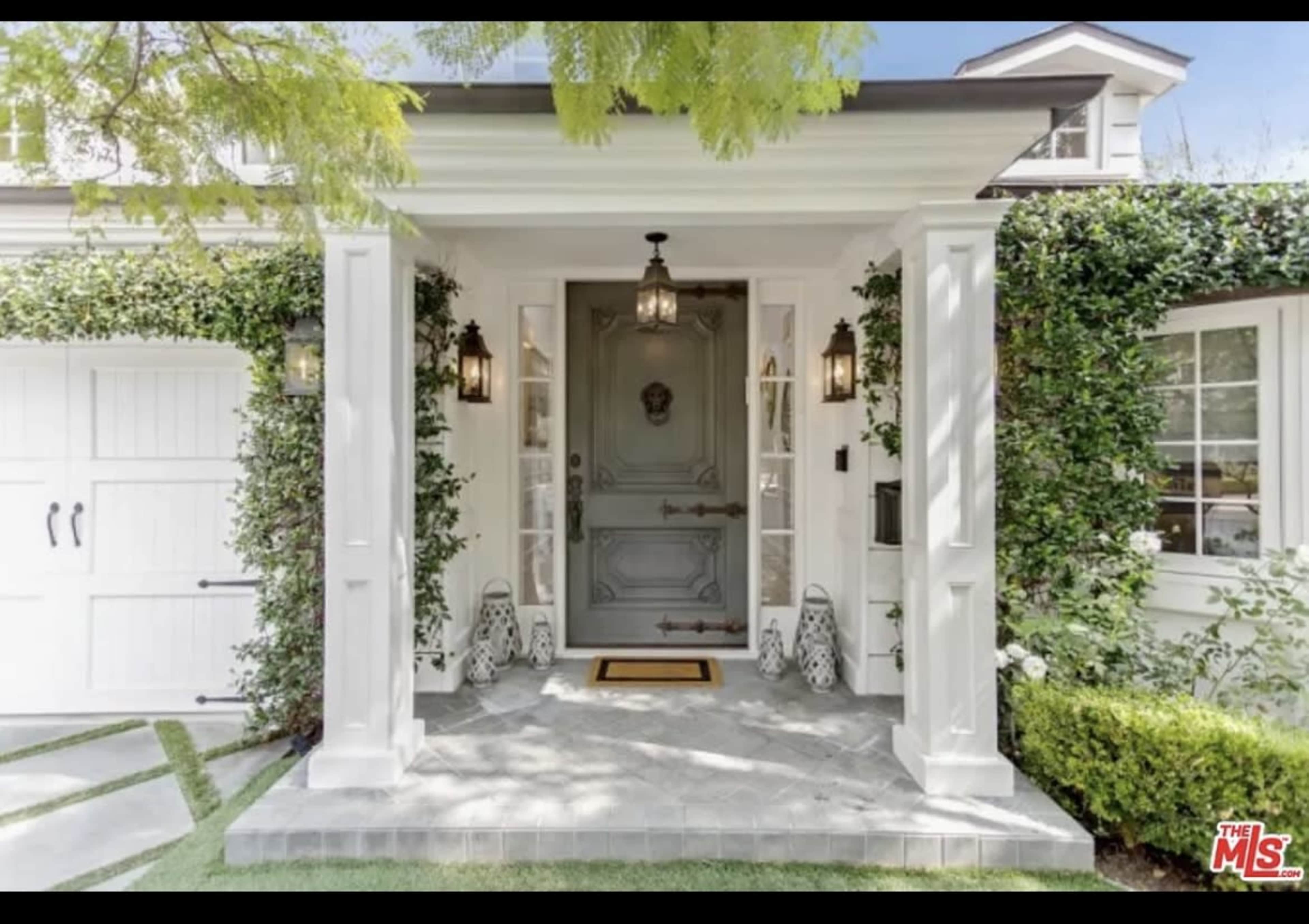 A modern home entrance featuring a gray front door flanked by decorative lanterns and surrounded by lush greenery.