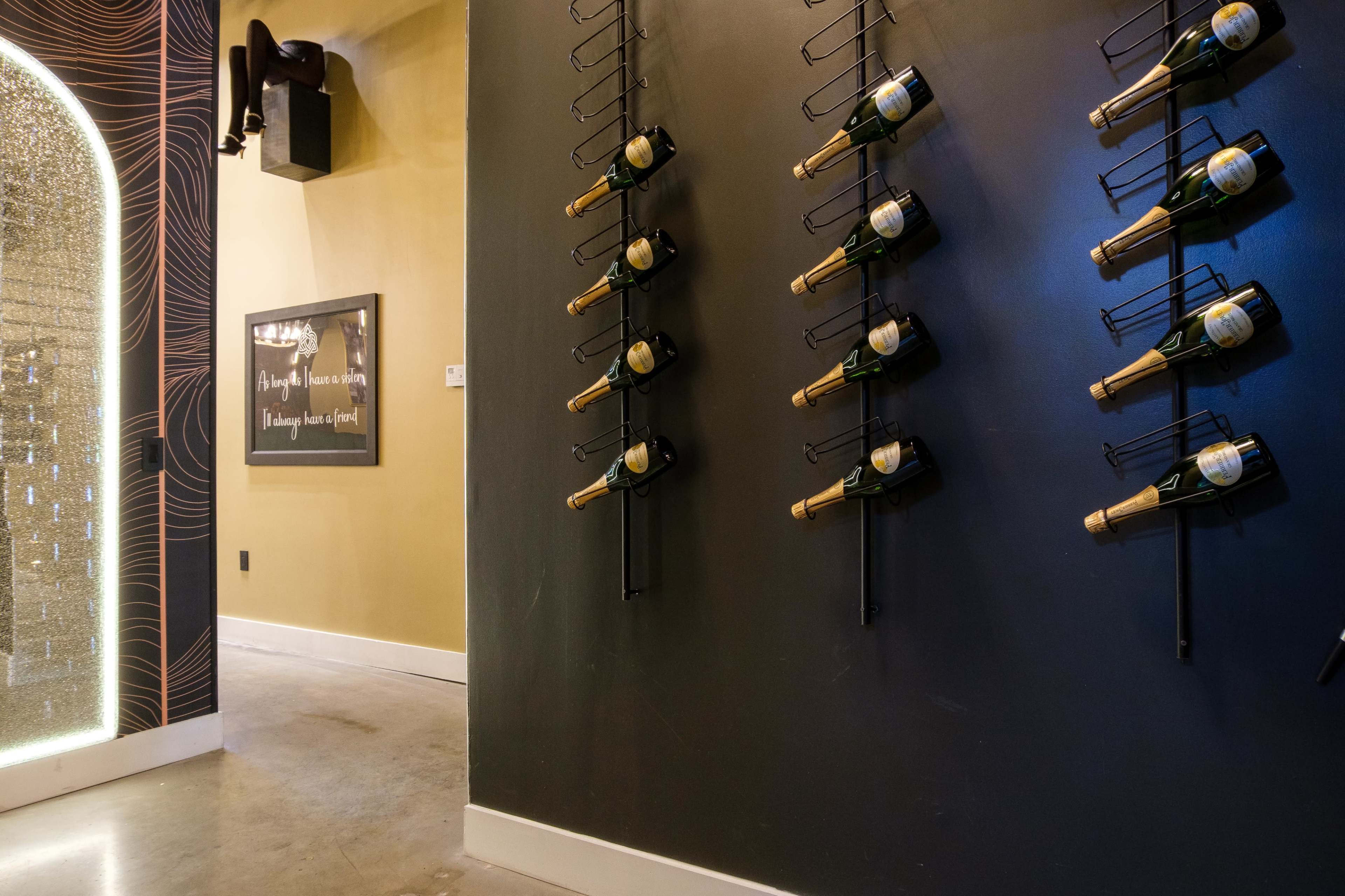 The image shows a wall displaying several bottles of champagne arranged in metal holders, with a doorway leading to another room in the background.