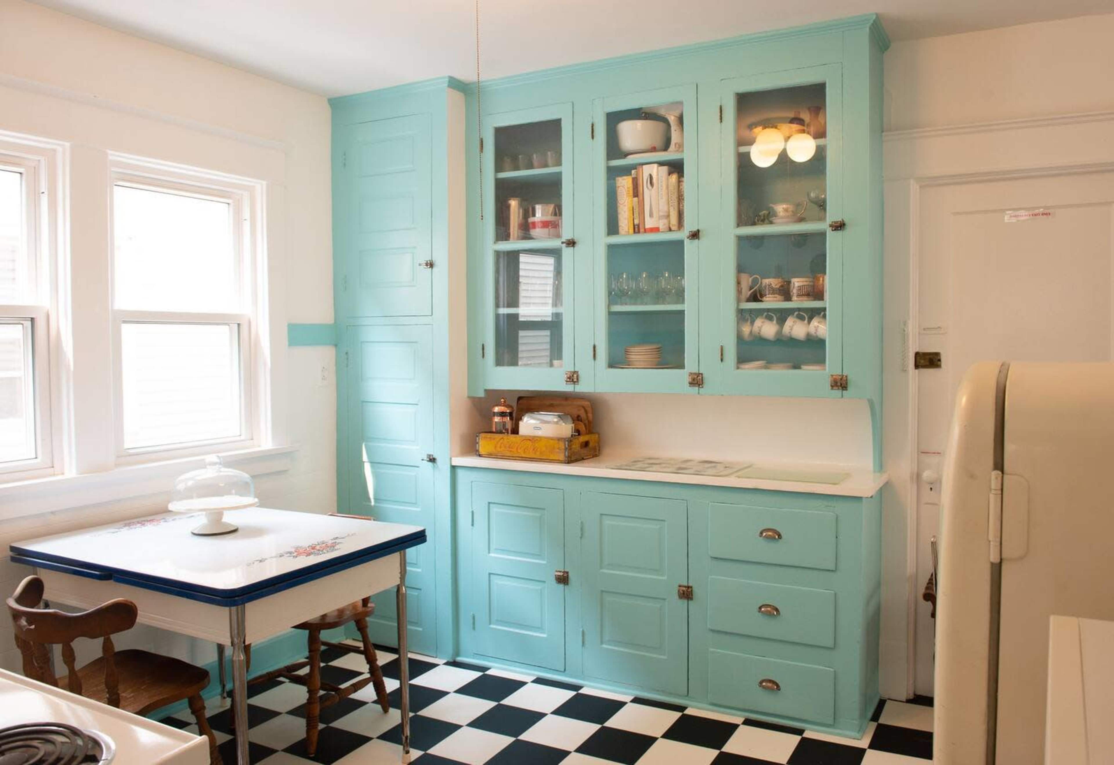 The kitchen features turquoise cabinets, a white table, and a black and white checkered floor.