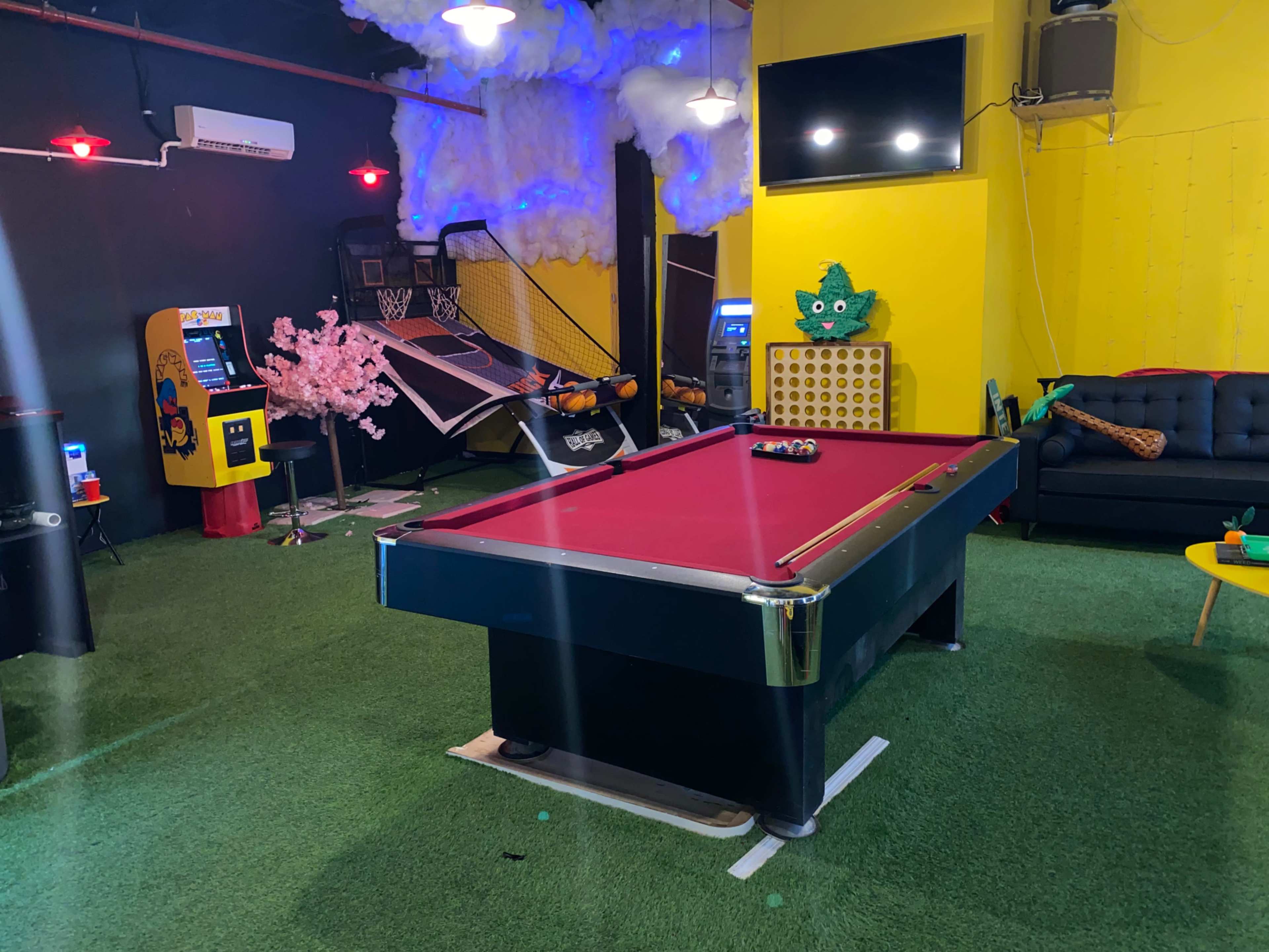 The room features a pool table at the center, surrounded by a basketball hoop, arcade game machine, and various seating and decorative elements.