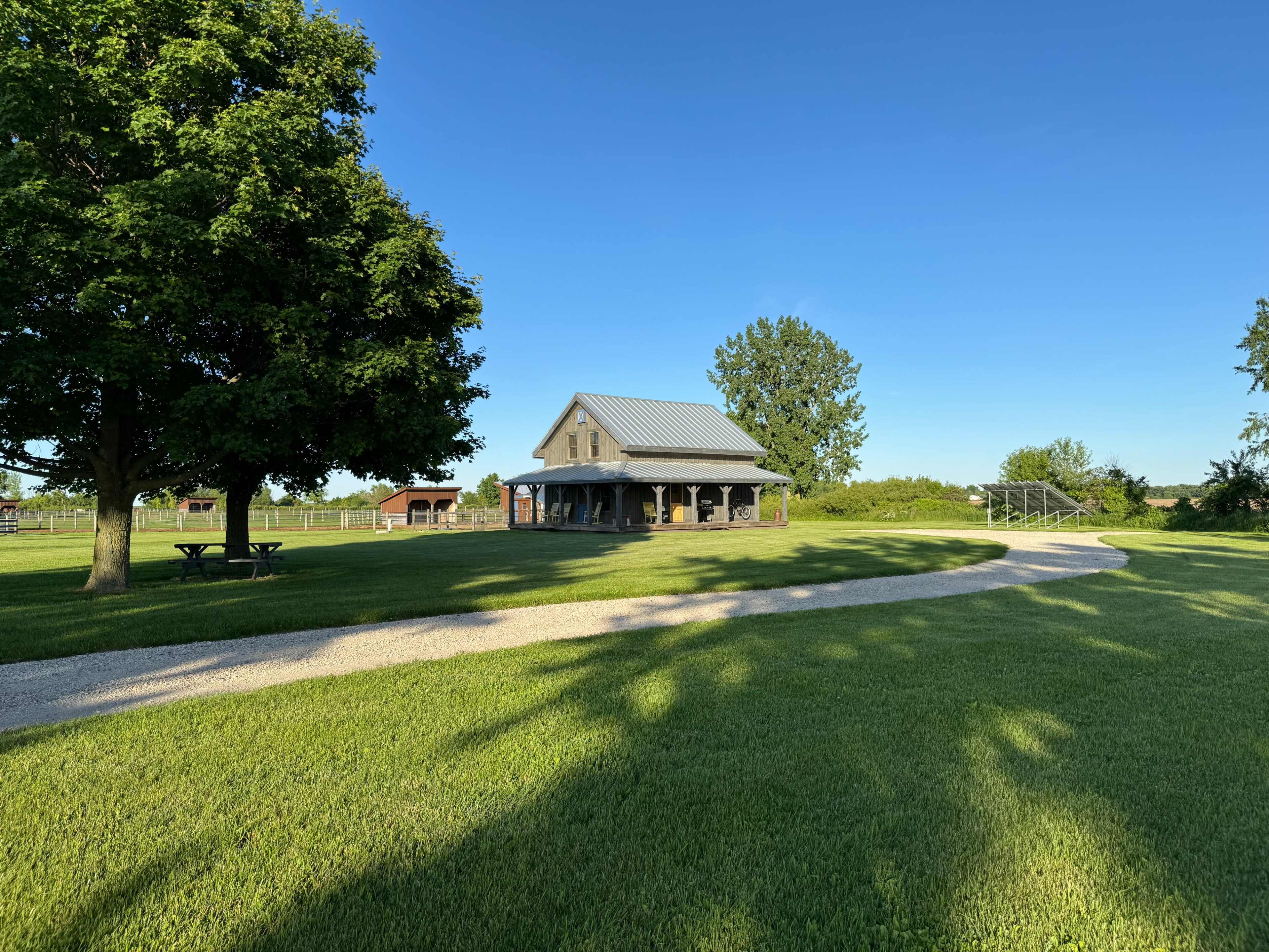 A well-maintained gravel path leads to a rustic building surrounded by green grass and trees under a clear blue sky.