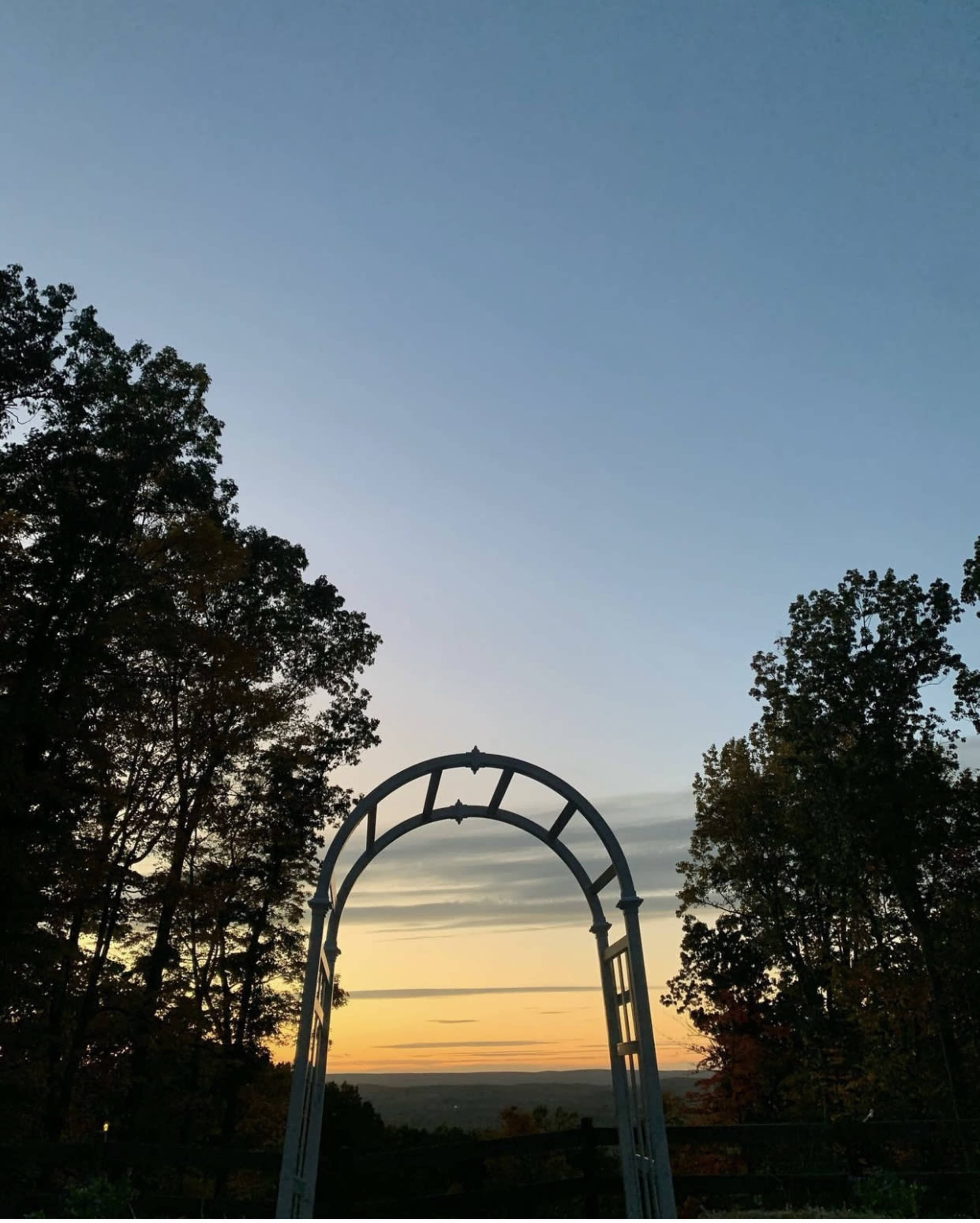An archway frames a view of a sunset over a horizon lined with trees.