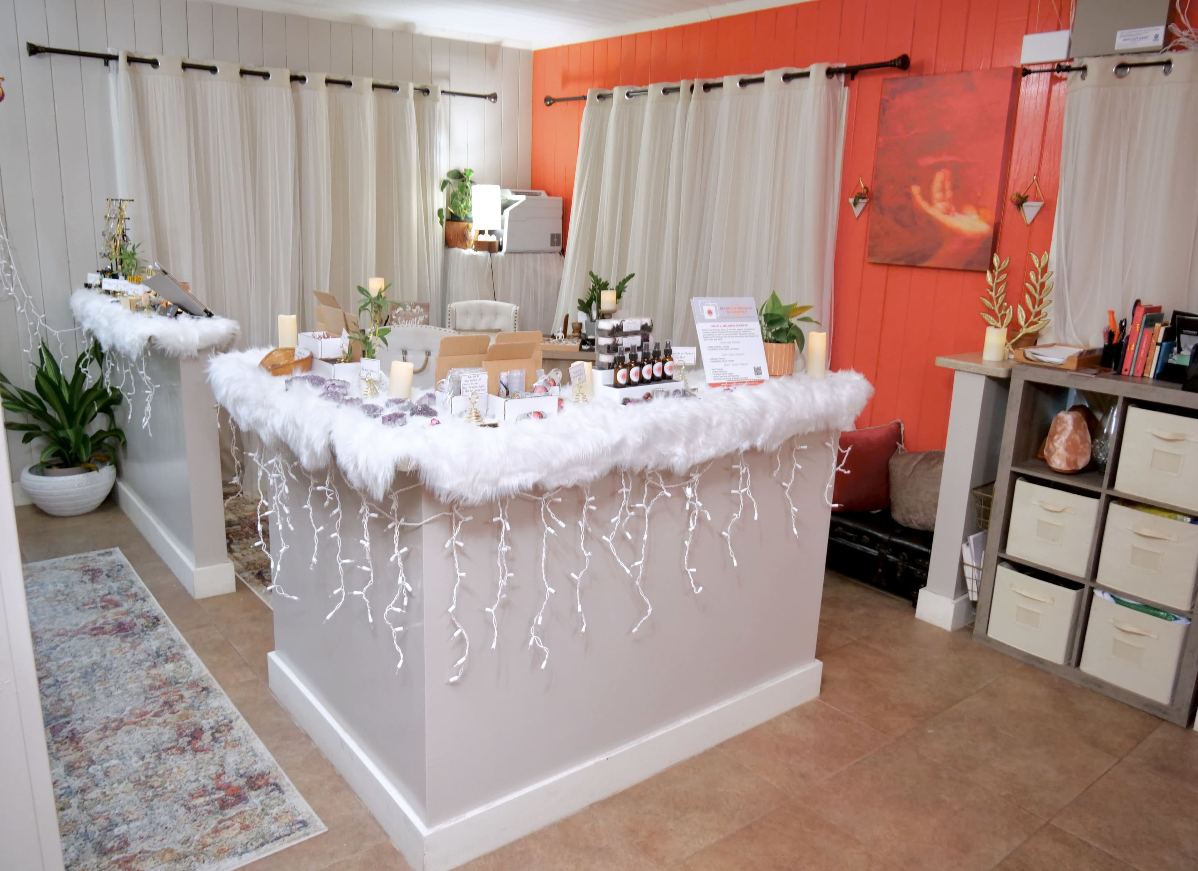 A cozy retail space with two counter displays adorned with white garland and candles, surrounded by plants and soft lighting.