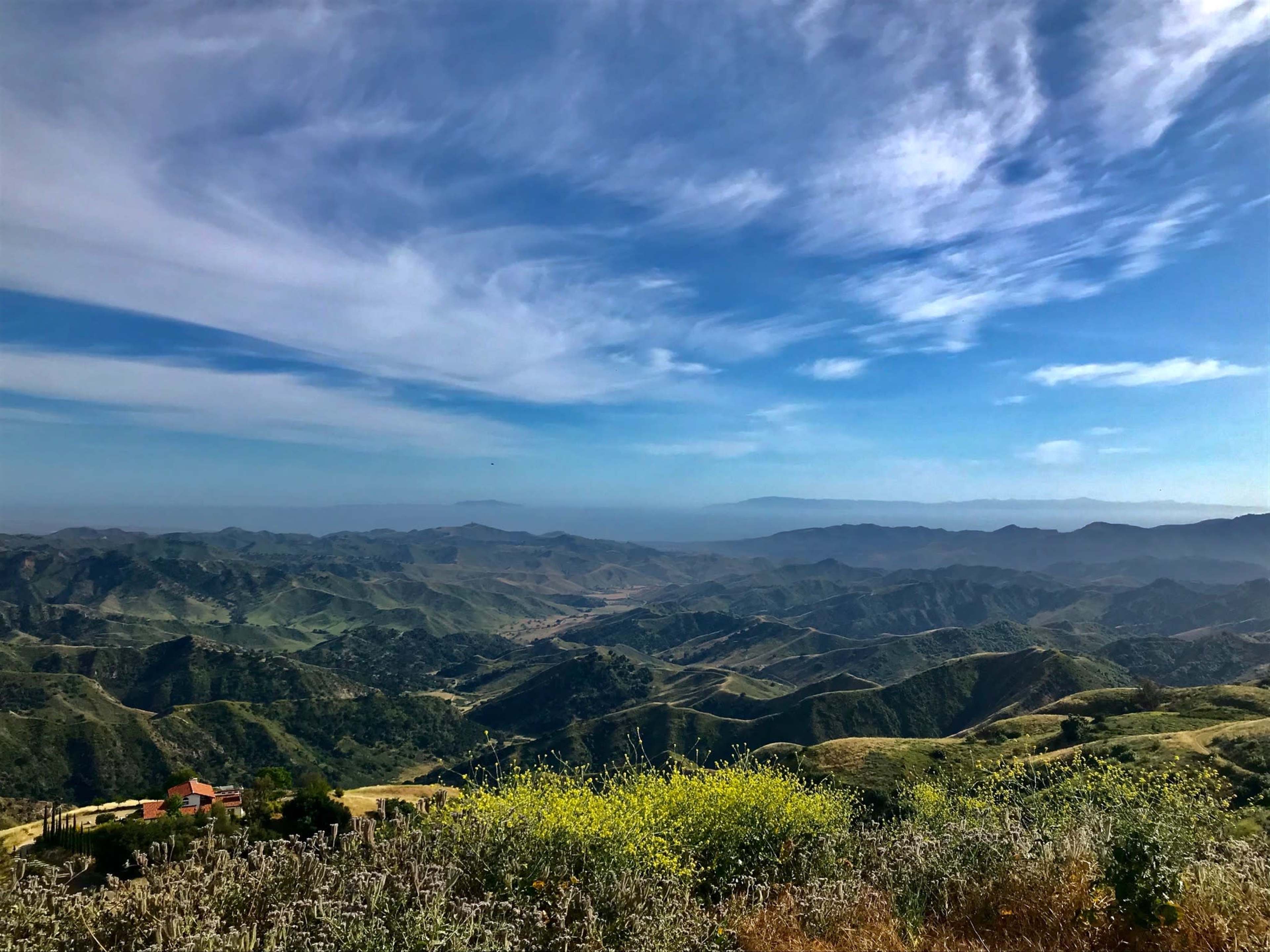 A panoramic view of rolling hills and valleys under a blue sky with scattered clouds.
