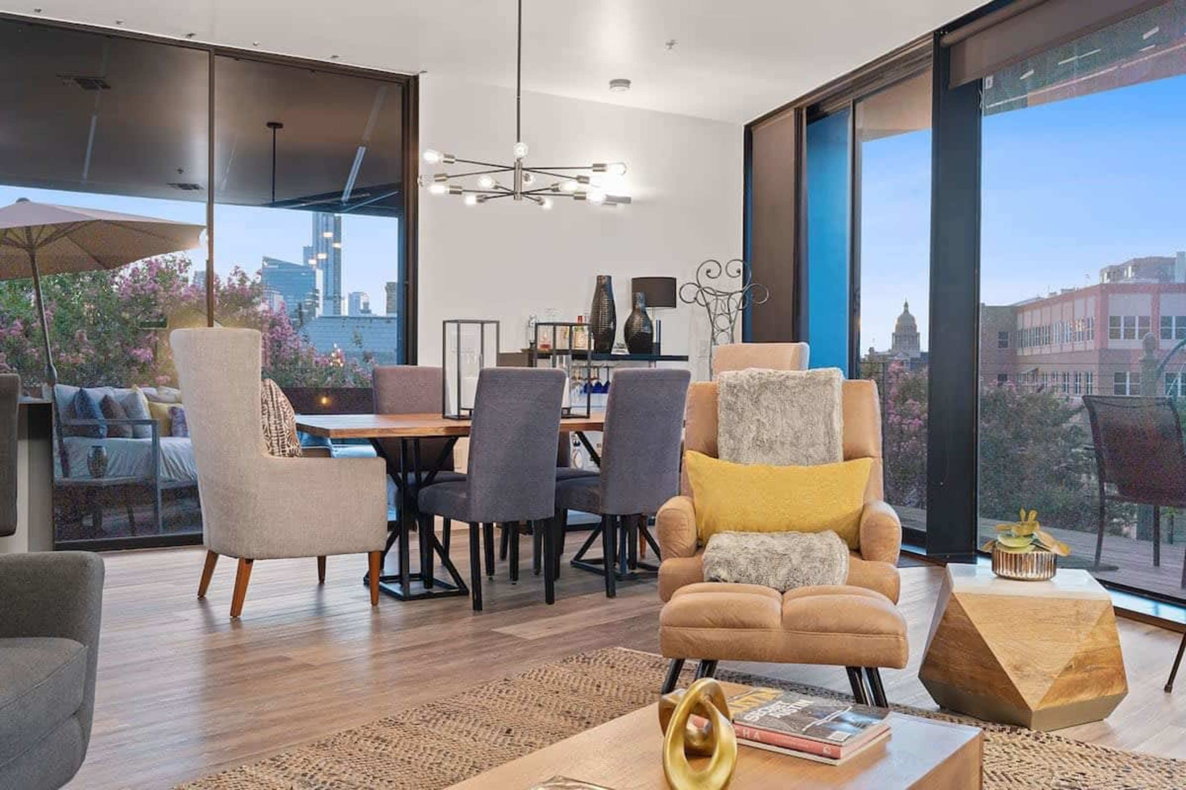 A modern interior of a living space with a dining area, comfortable seating, and large windows overlooking a city view.