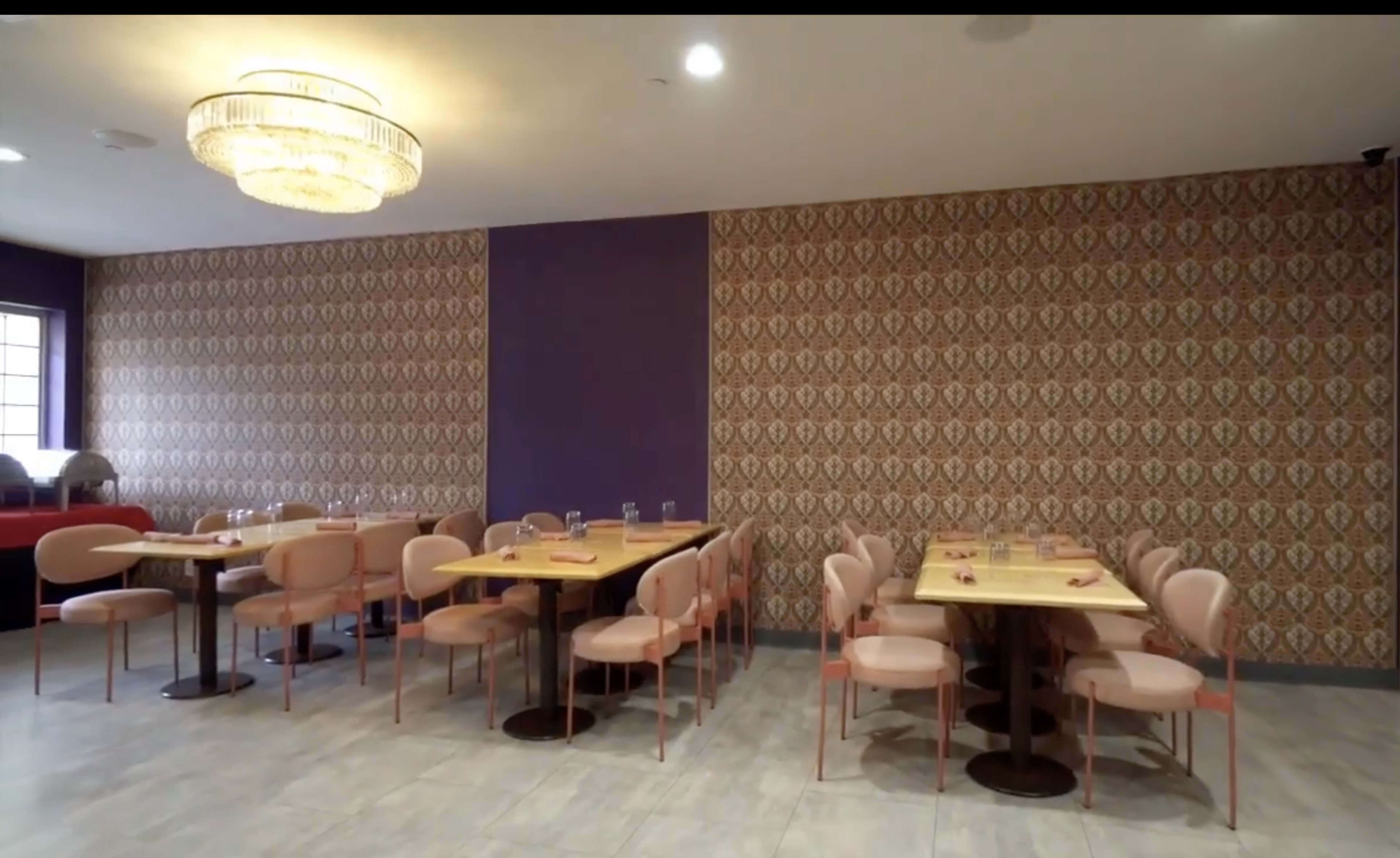The image shows a modern restaurant interior featuring several tables with pink chairs against a patterned wallpaper and purple accent wall.